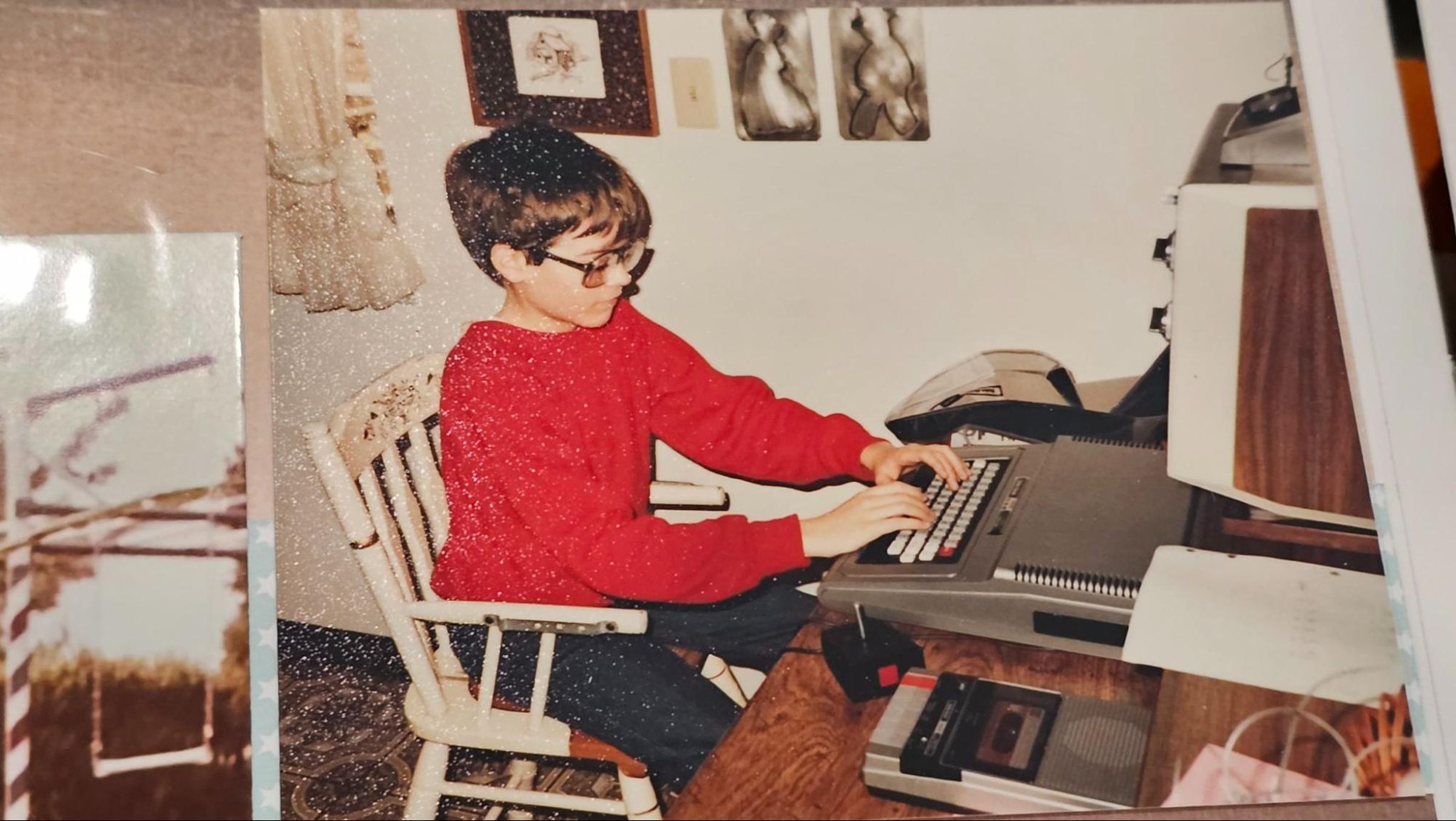 kid on white wooden chair in front of computer desk wearing red shirt and using computer