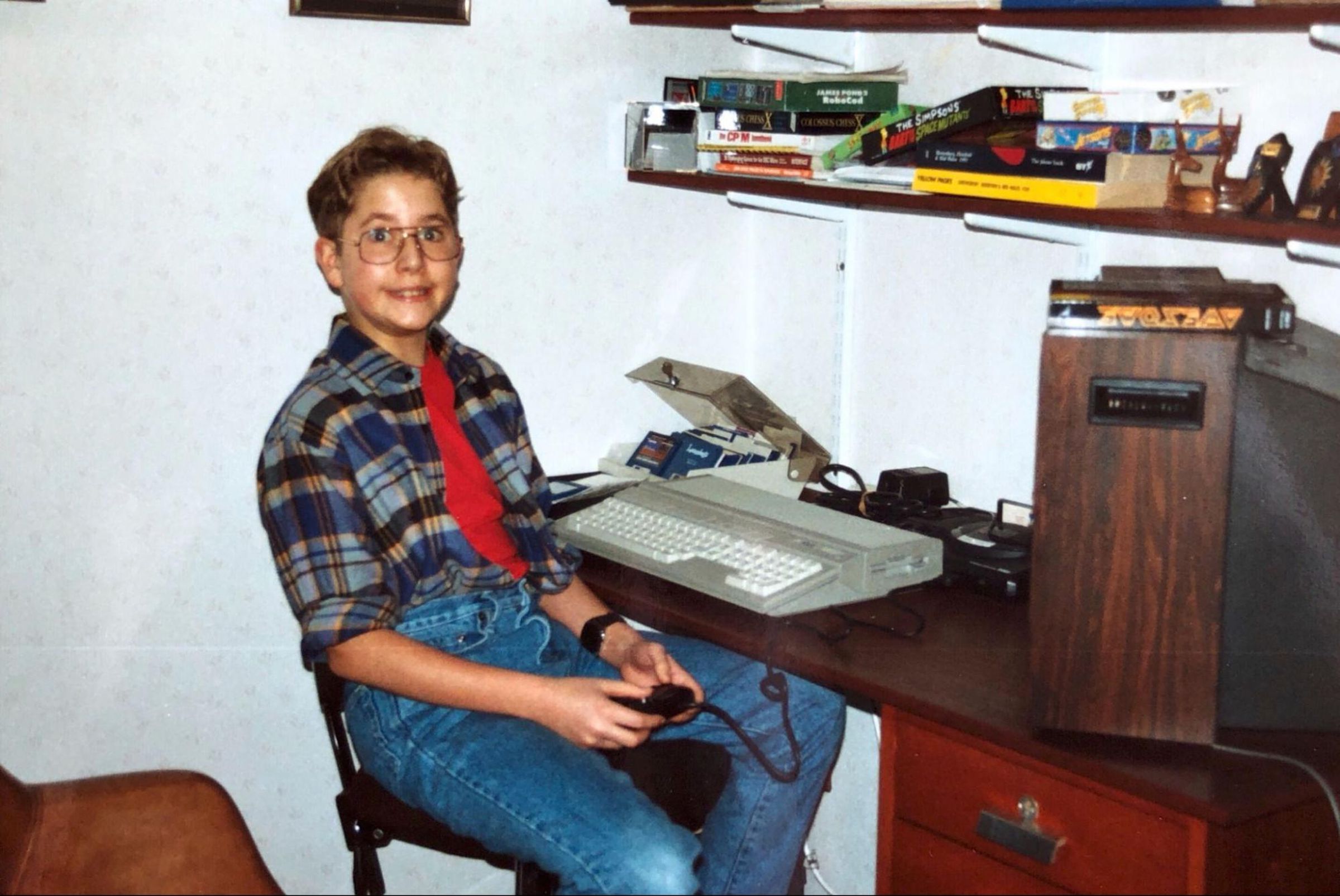 kid at desk playing Sega with atari st on the desk and a case of floppies.