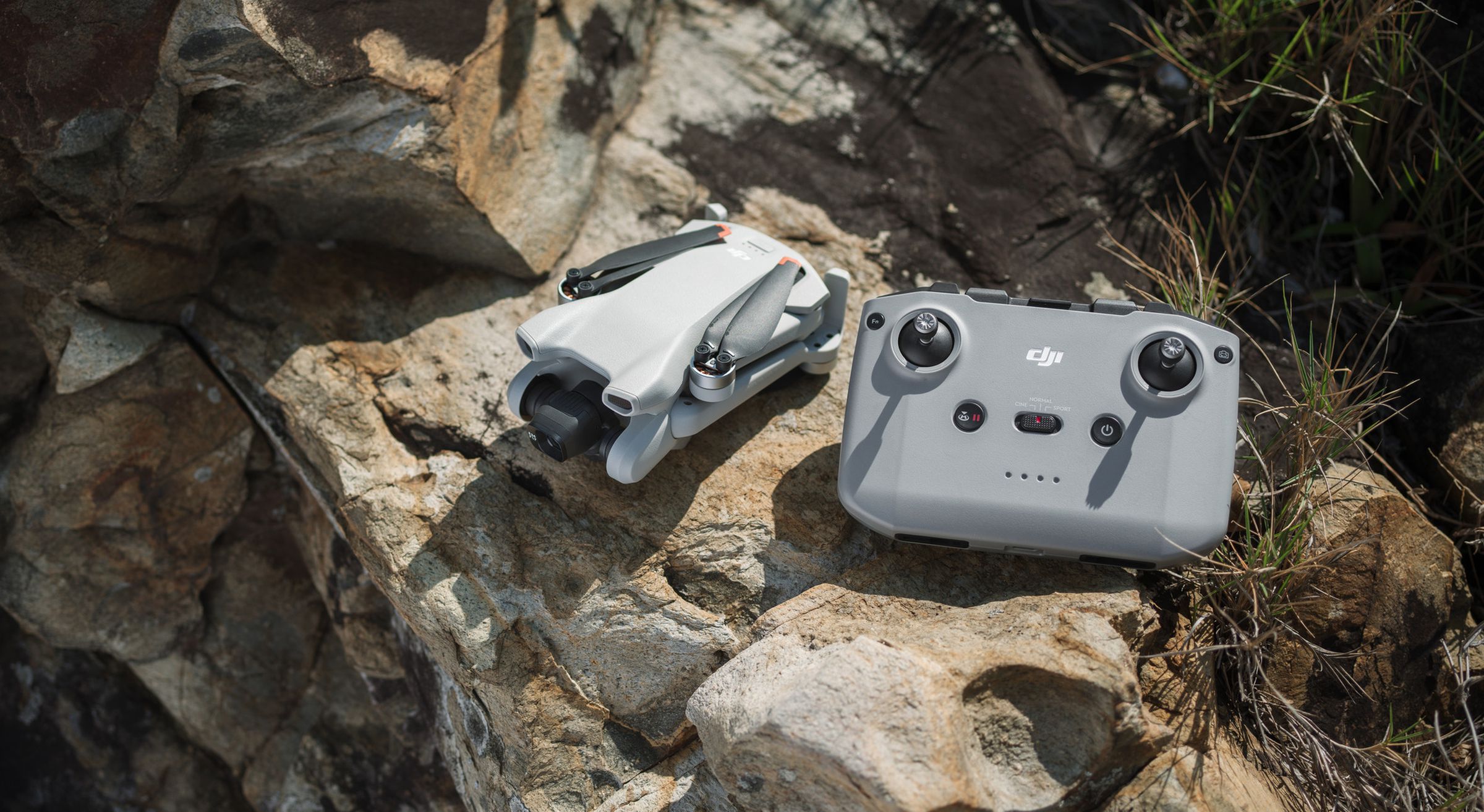 Le drone DJI Mini 3 sans les pales étendu à côté du contrôleur DJI RC-N1.  Les deux produits reposent sur un gros rocher dans un environnement extérieur.