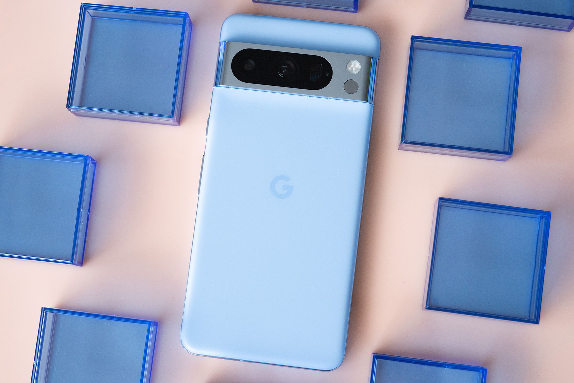Google Pixel 8 Pro in bay blue on a light pink background surrounded by blue plastic squares