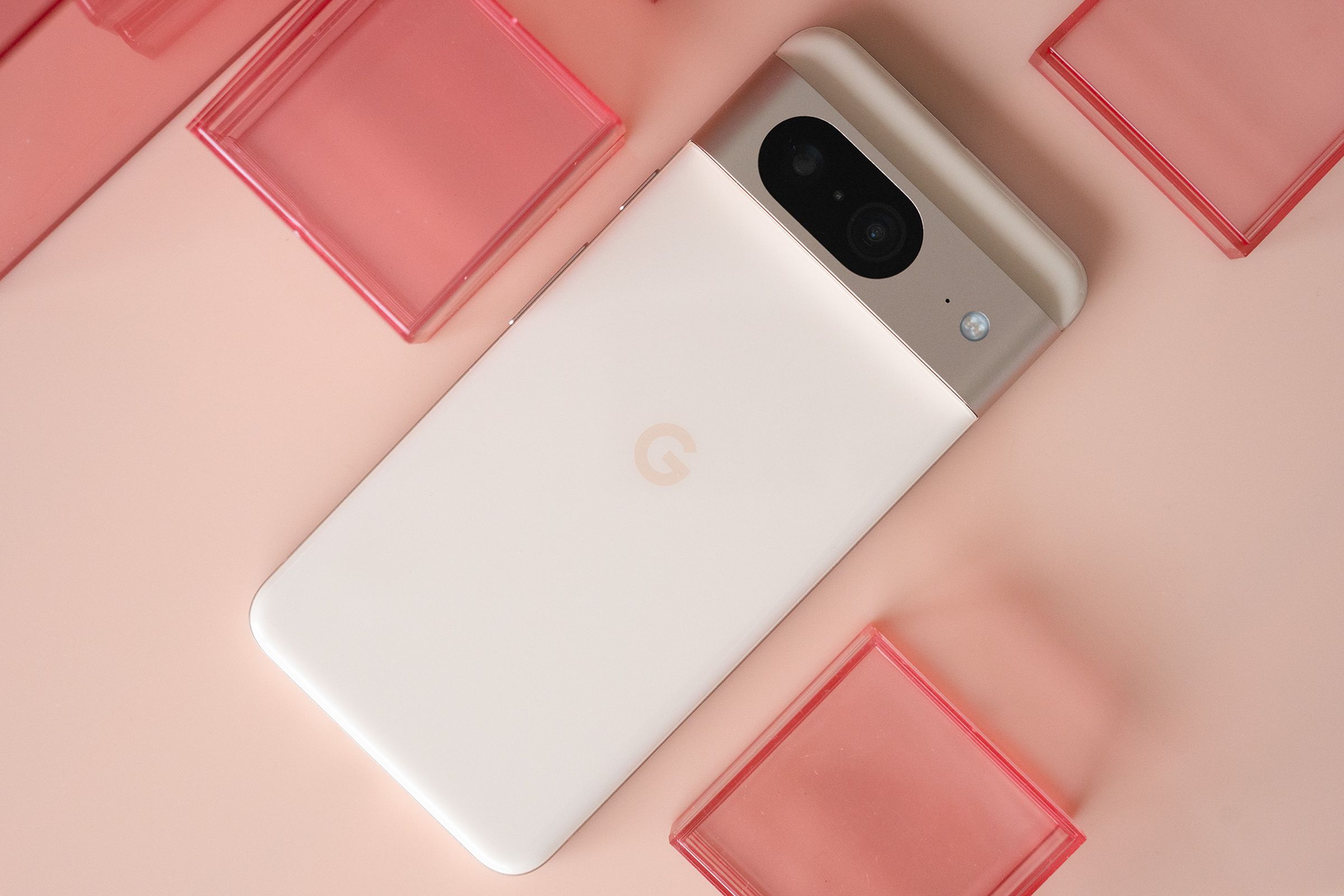 Google Pixel 8 with rear panel facing up in pink on a light pink background with red plastic cubes