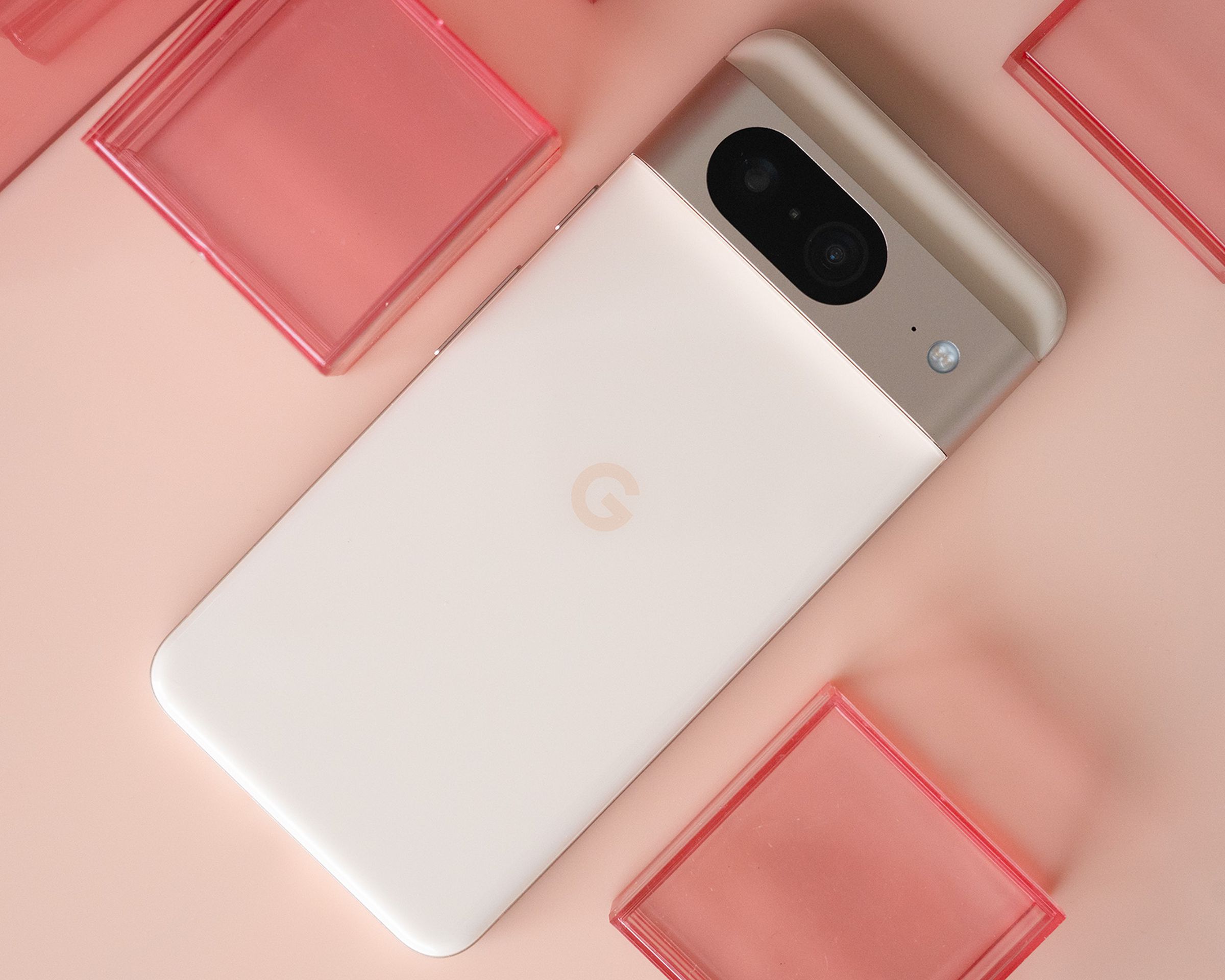 Google Pixel 8 with rear panel facing up in pink on a light pink background with red plastic cubes