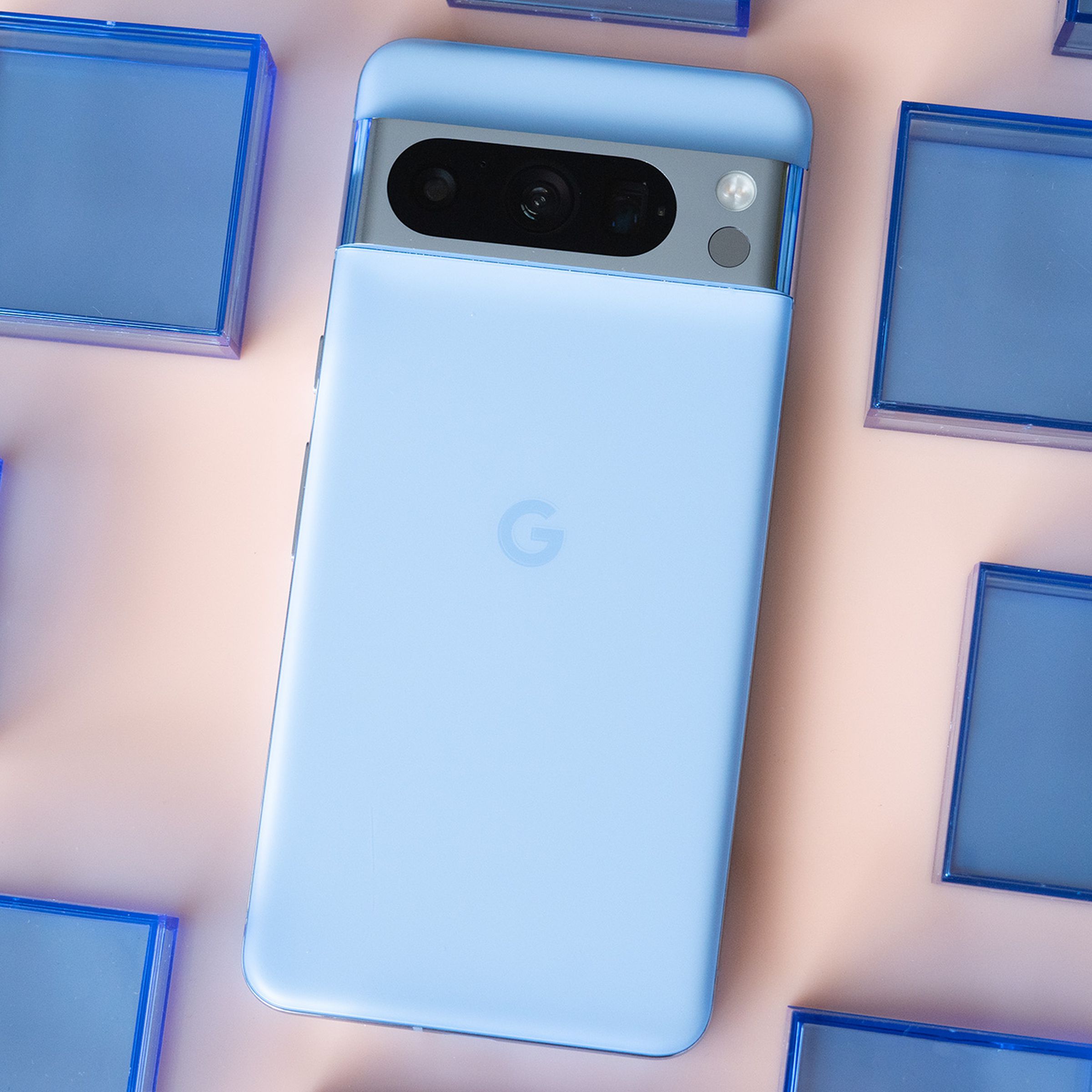 Google Pixel 8 Pro in bay blue on a light pink background surrounded by blue plastic squares