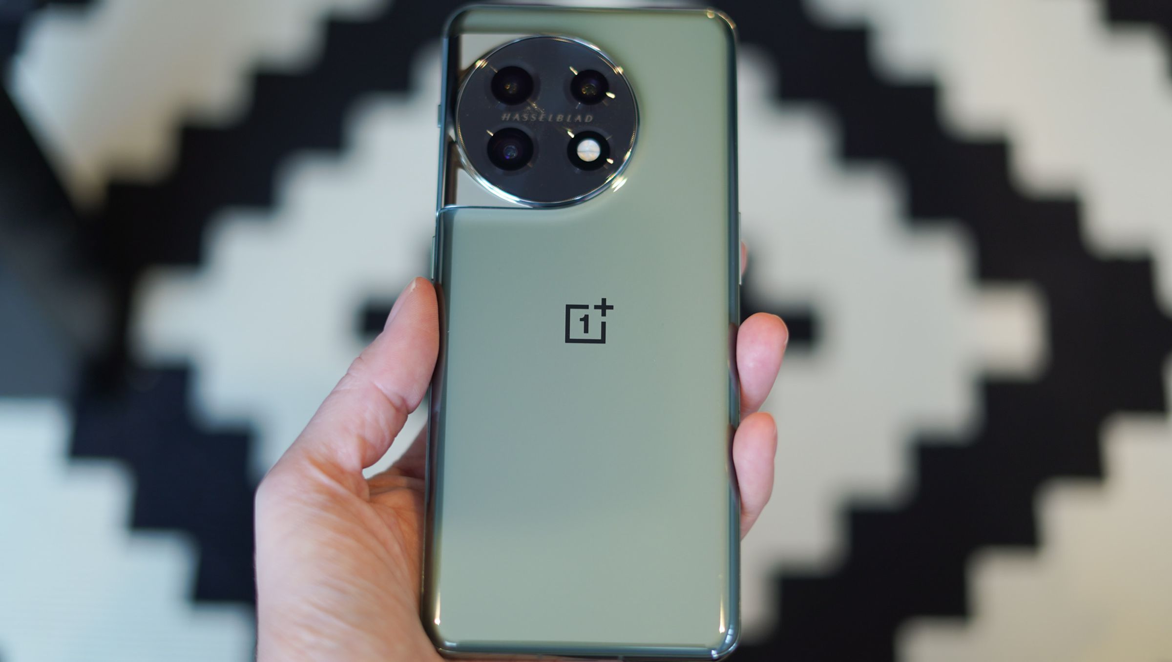OnePlus 11 5G in-hand showing green color option and OnePlus logo with a black and white background.