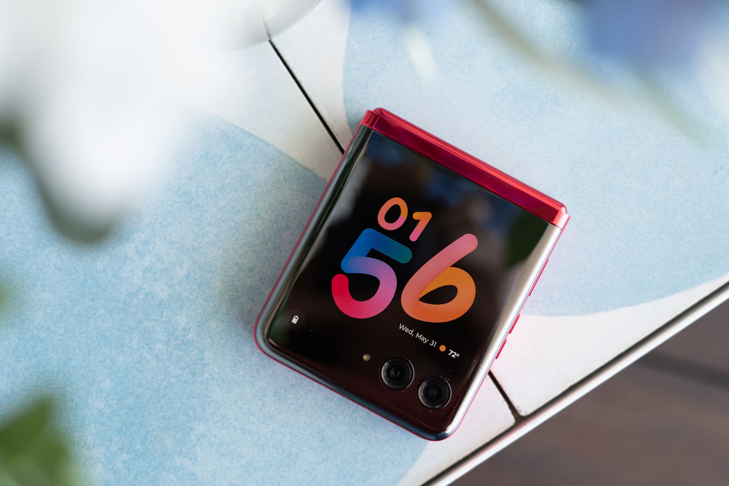 Motorola Razr Plus on a table top showing colorful clockface on cover screen.