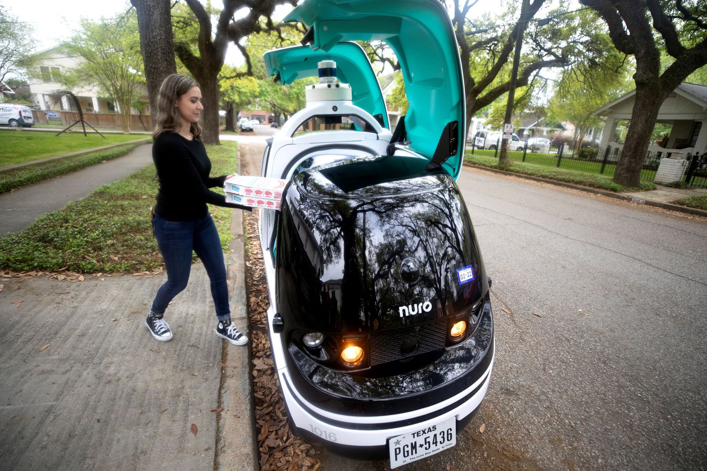 A customer retrieves her pizzas from Nuro’s R2 delivery robot.