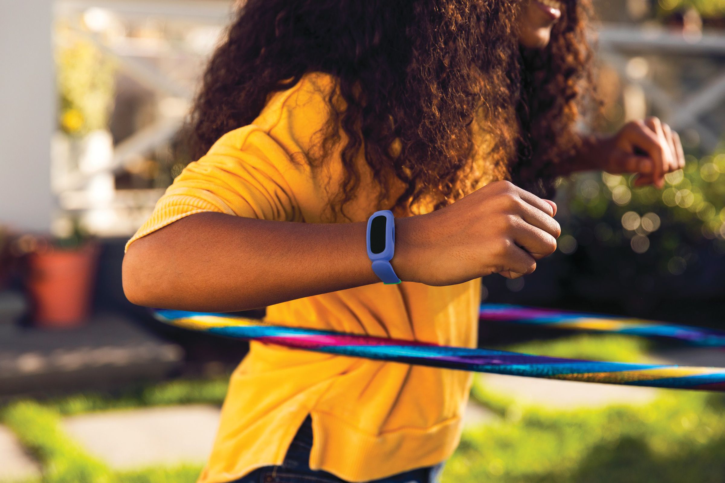 Sağ bileğinde mavi bir Fitbit Ace takarken hulahup atan bir çocuğun fotoğrafı.