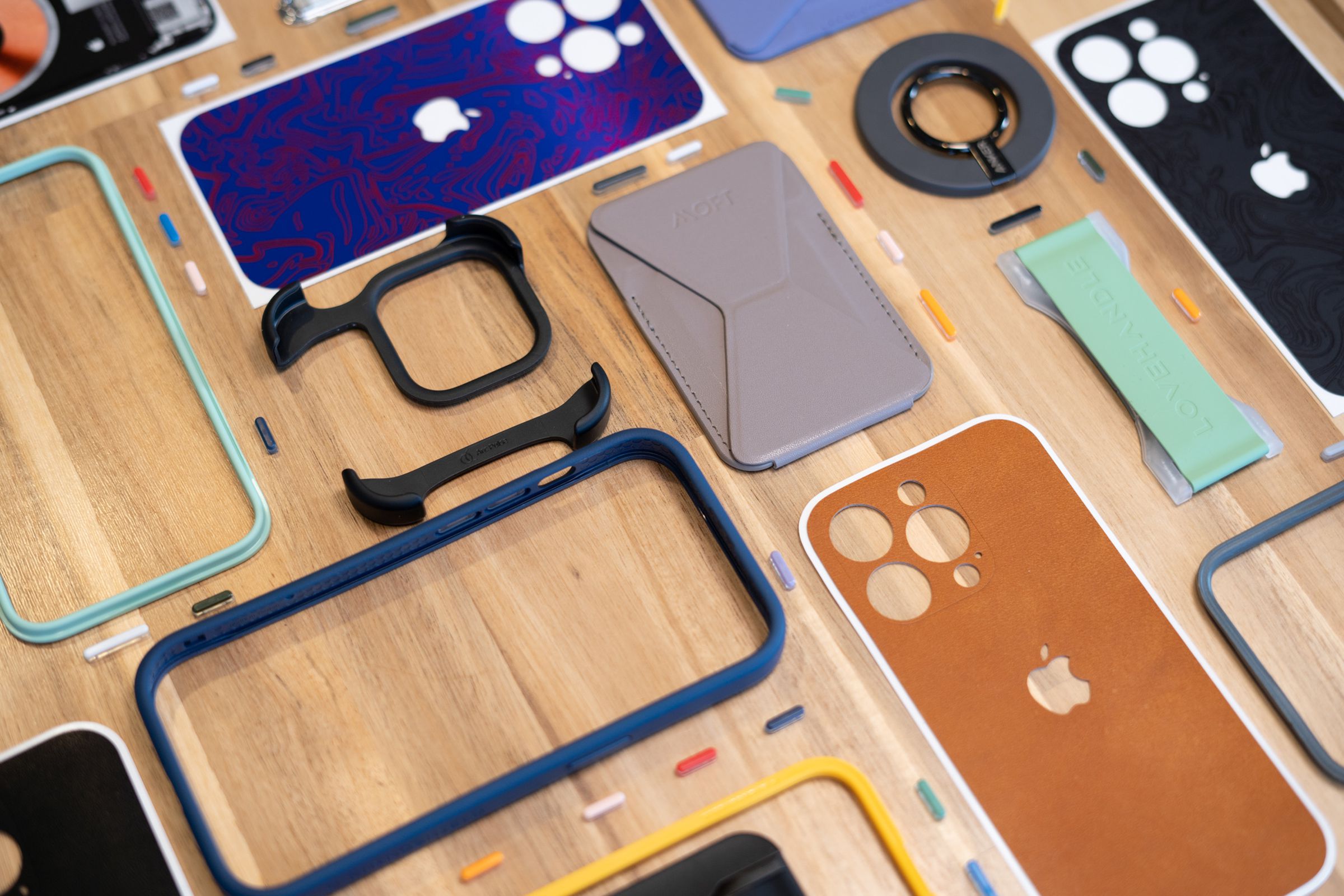 A set of wallets, grips, and colorful phone bumper cases with interchangeable buttons laid out on a table.