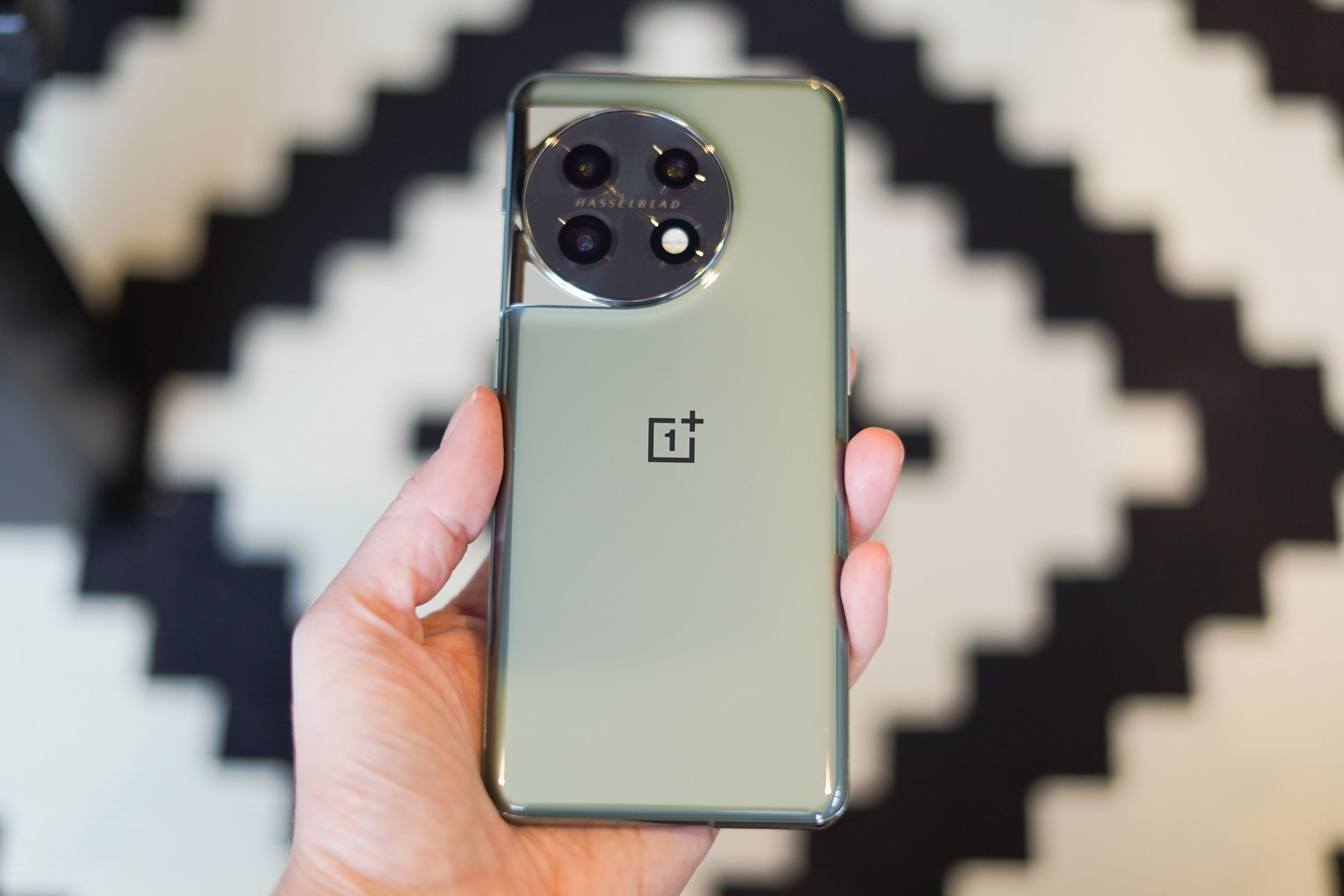 OnePlus in hand showing back panel against a black and white patterned background.