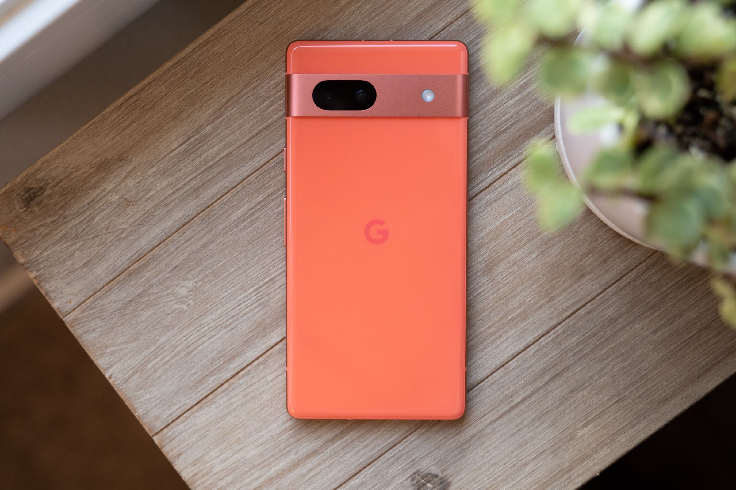 Google Pixel 7A in coral on a wooden table showing rear panel.