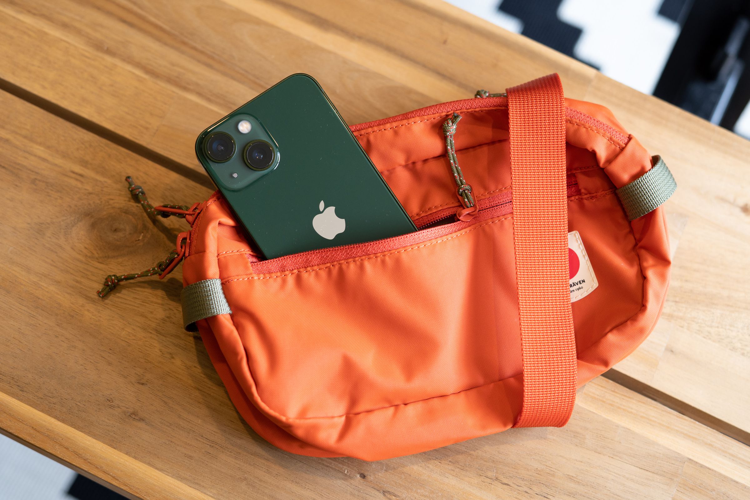 iPhone 13 Mini in the front pocket of an orange belt bag.