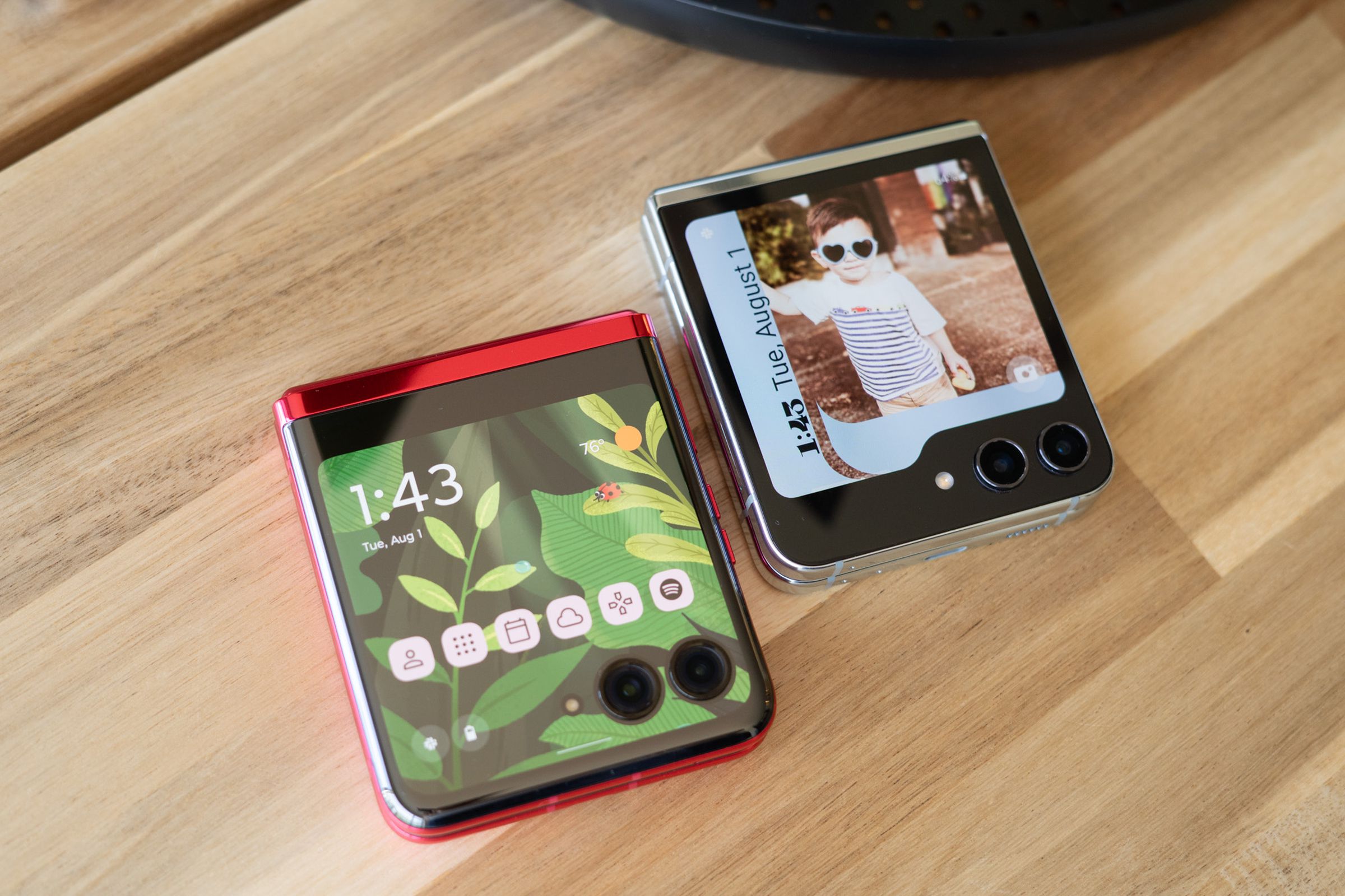 Photo showing Motorola Razr Plus and Samsung Galaxy Z Flip 5 on a tabletop showing cover display home screens.