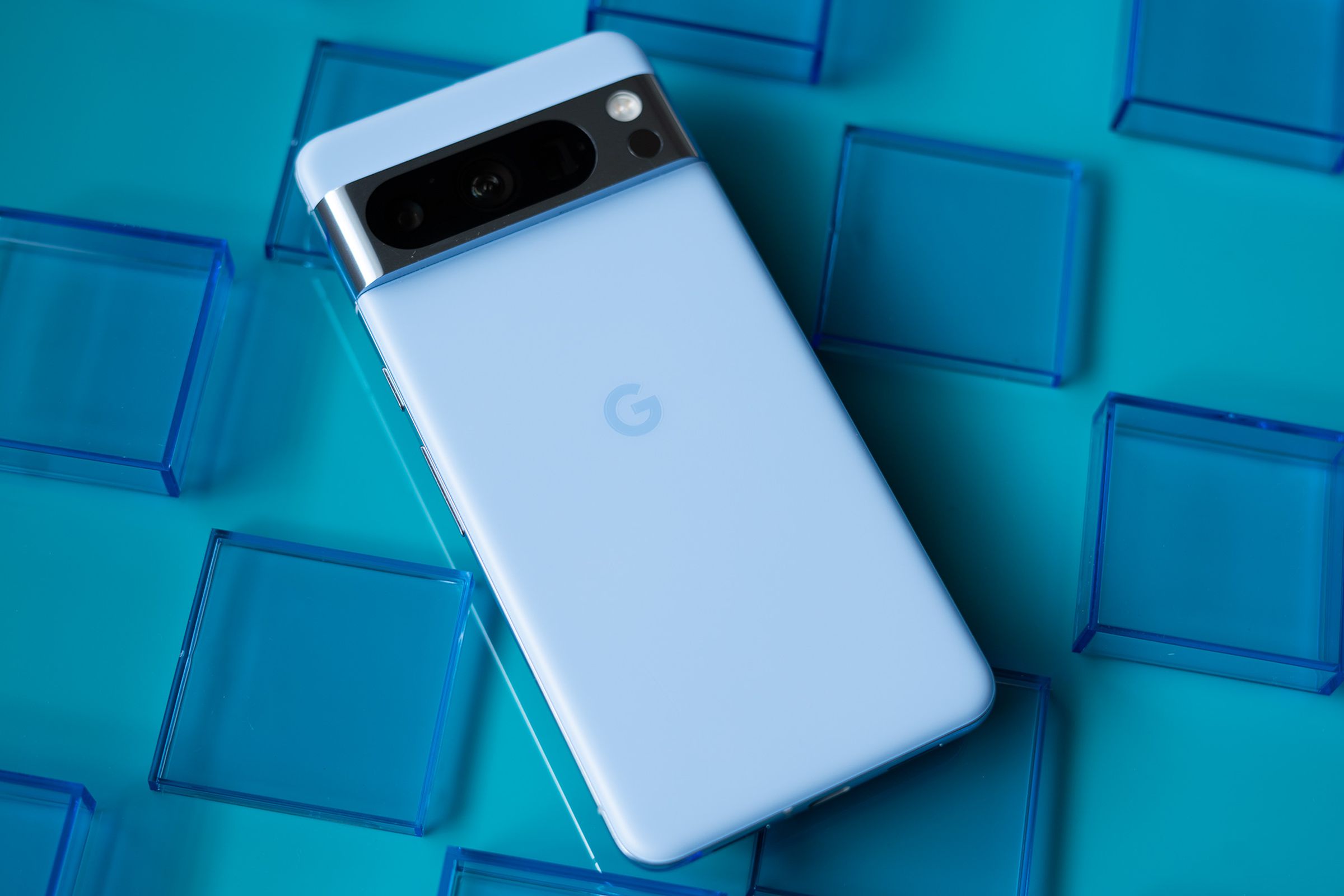 Google Pixel 8 Pro in bay blue showing back panel on a teal blue background surrounded by transparent blue squares