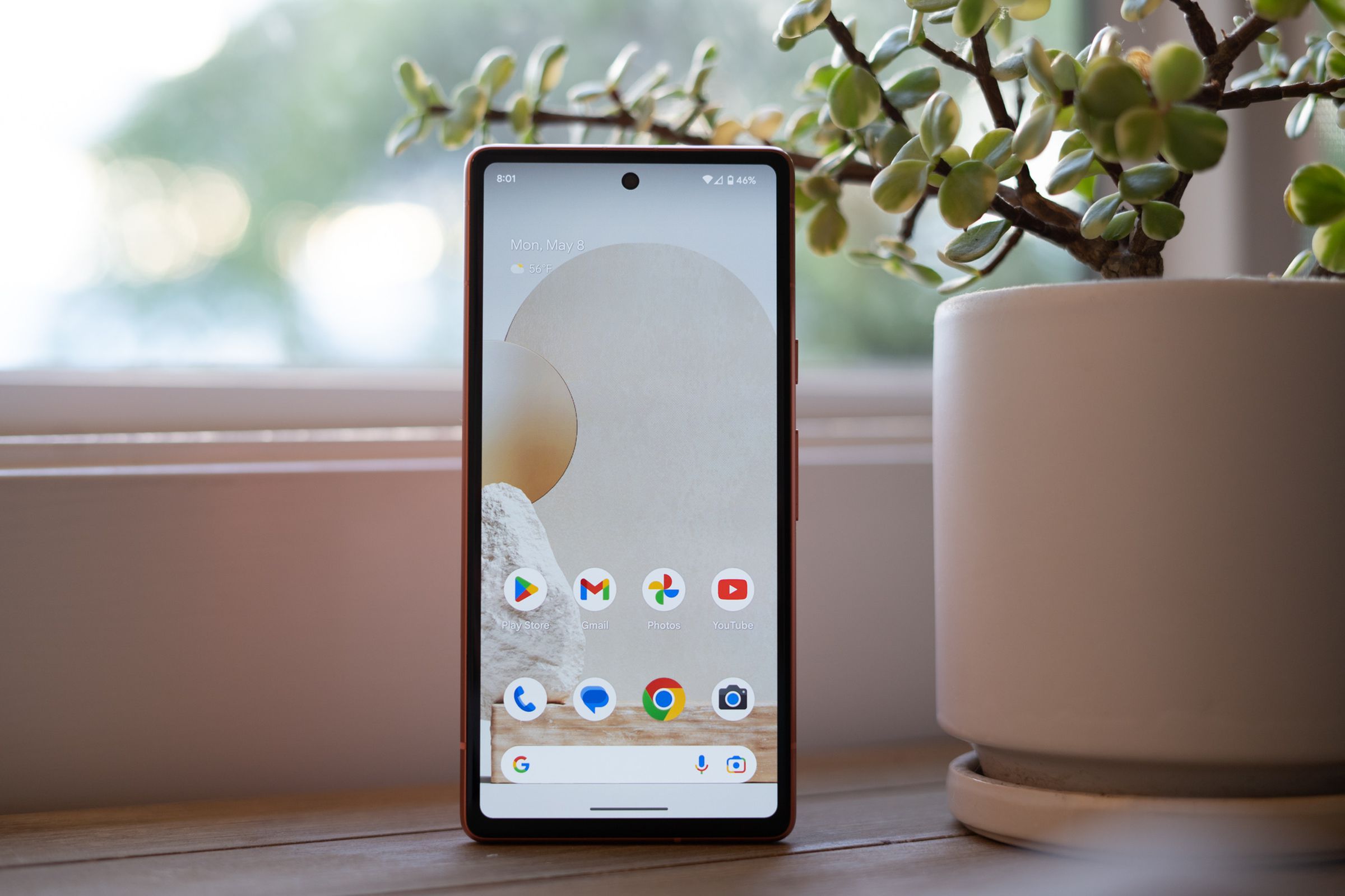 Google Pixel 7A standing upright on a table showing home screen.