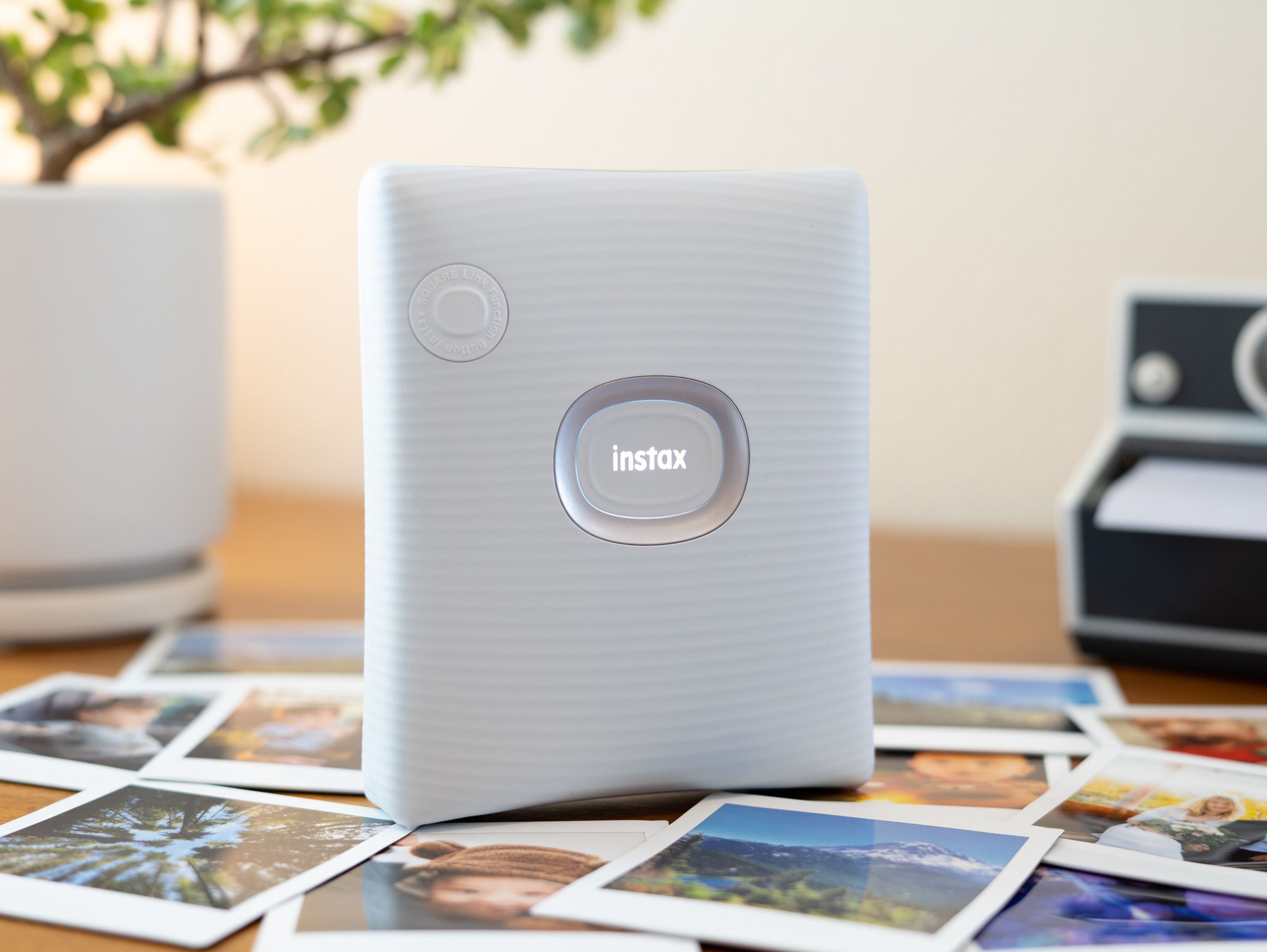 Instax Square Link standing upright with logo illuminated on a desk with square prints.