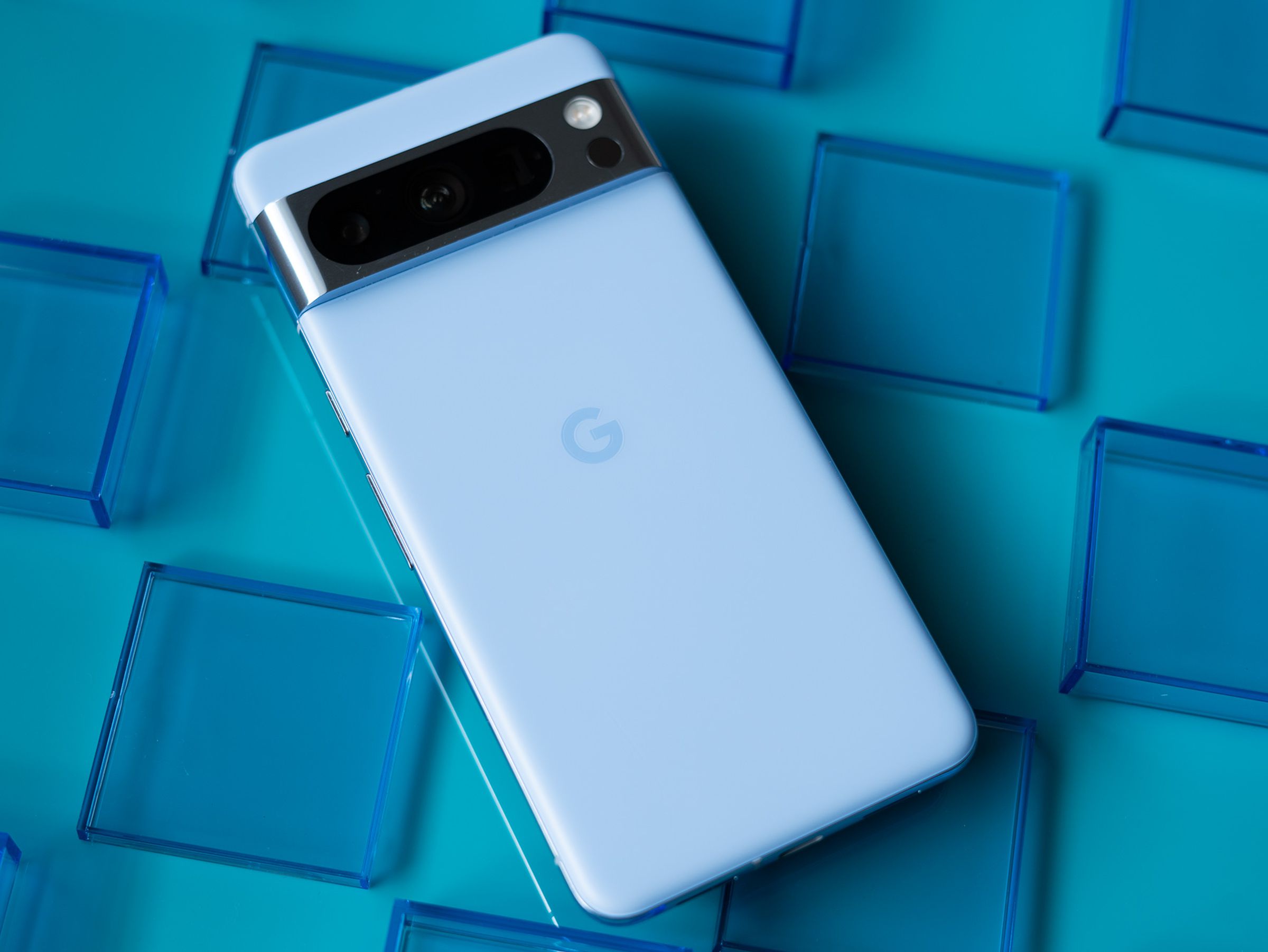 Google Pixel 8 Pro in bay blue showing back panel on a teal blue background surrounded by transparent blue squares