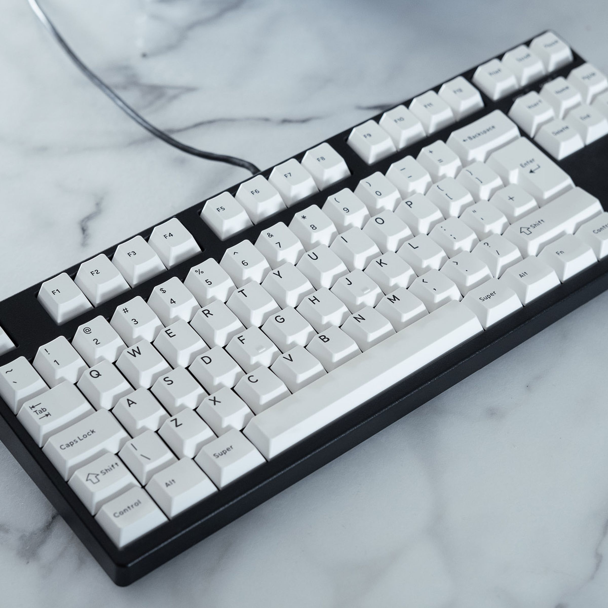 A black mechanical keyboard with white keycaps on a white marble table.
