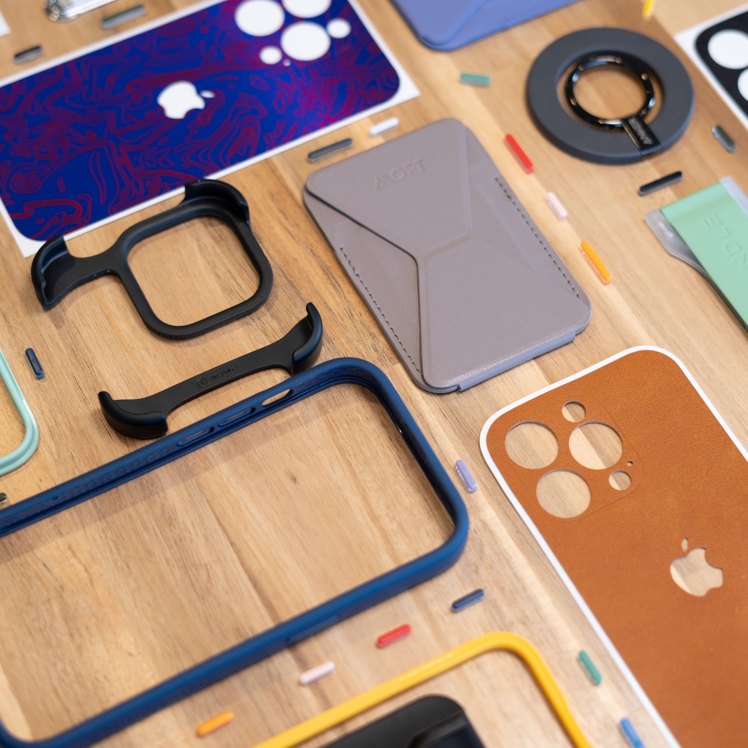 A set of wallets, grips, and colorful phone bumper cases with interchangeable buttons laid out on a table.