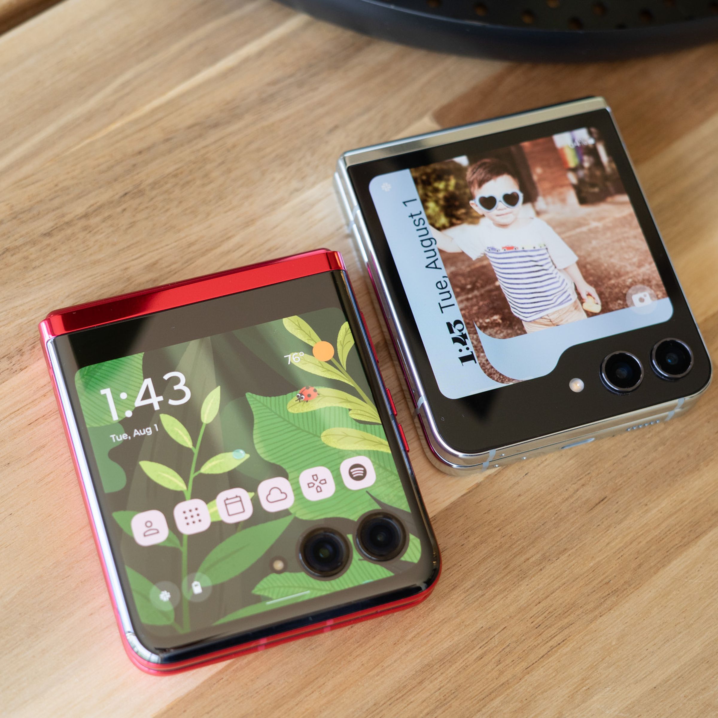 Photo showing Motorola Razr Plus and Samsung Galaxy Z Flip 5 on a tabletop showing cover display home screens.
