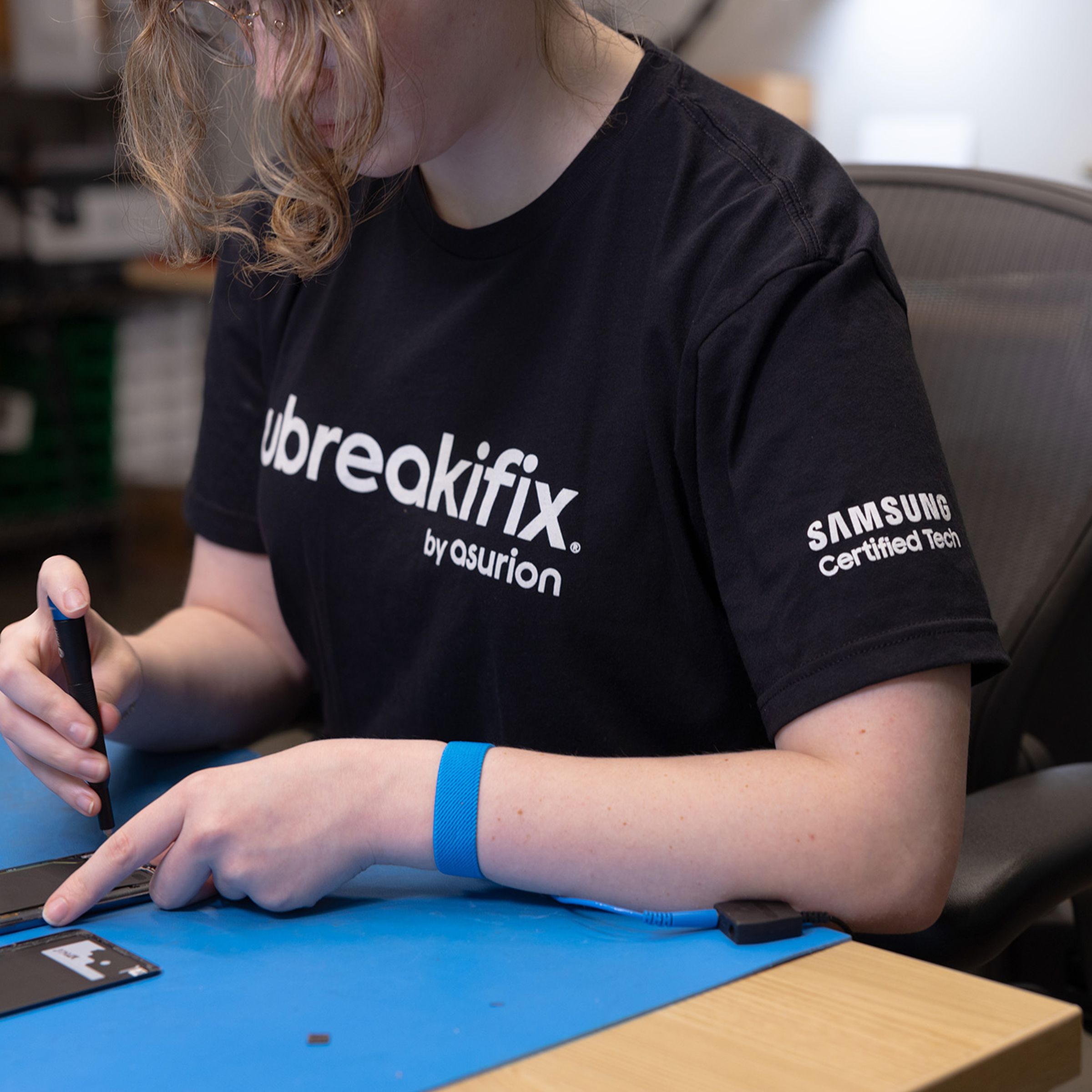 Image of a woman in an uBreakiFix shirt repairing a phone
