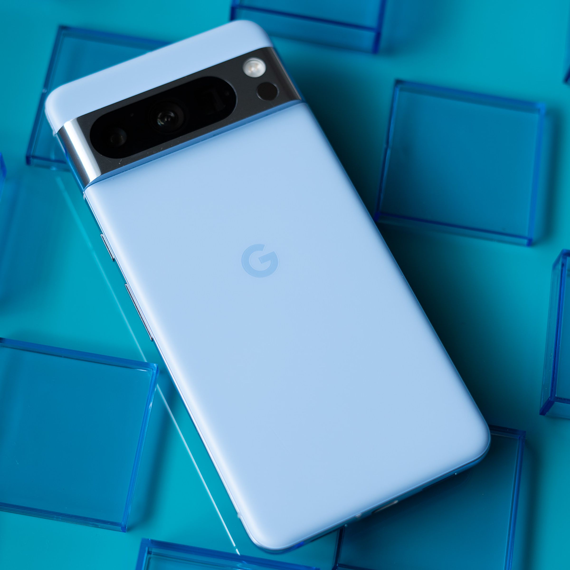Google Pixel 8 Pro in bay blue showing back panel on a teal blue background surrounded by transparent blue squares