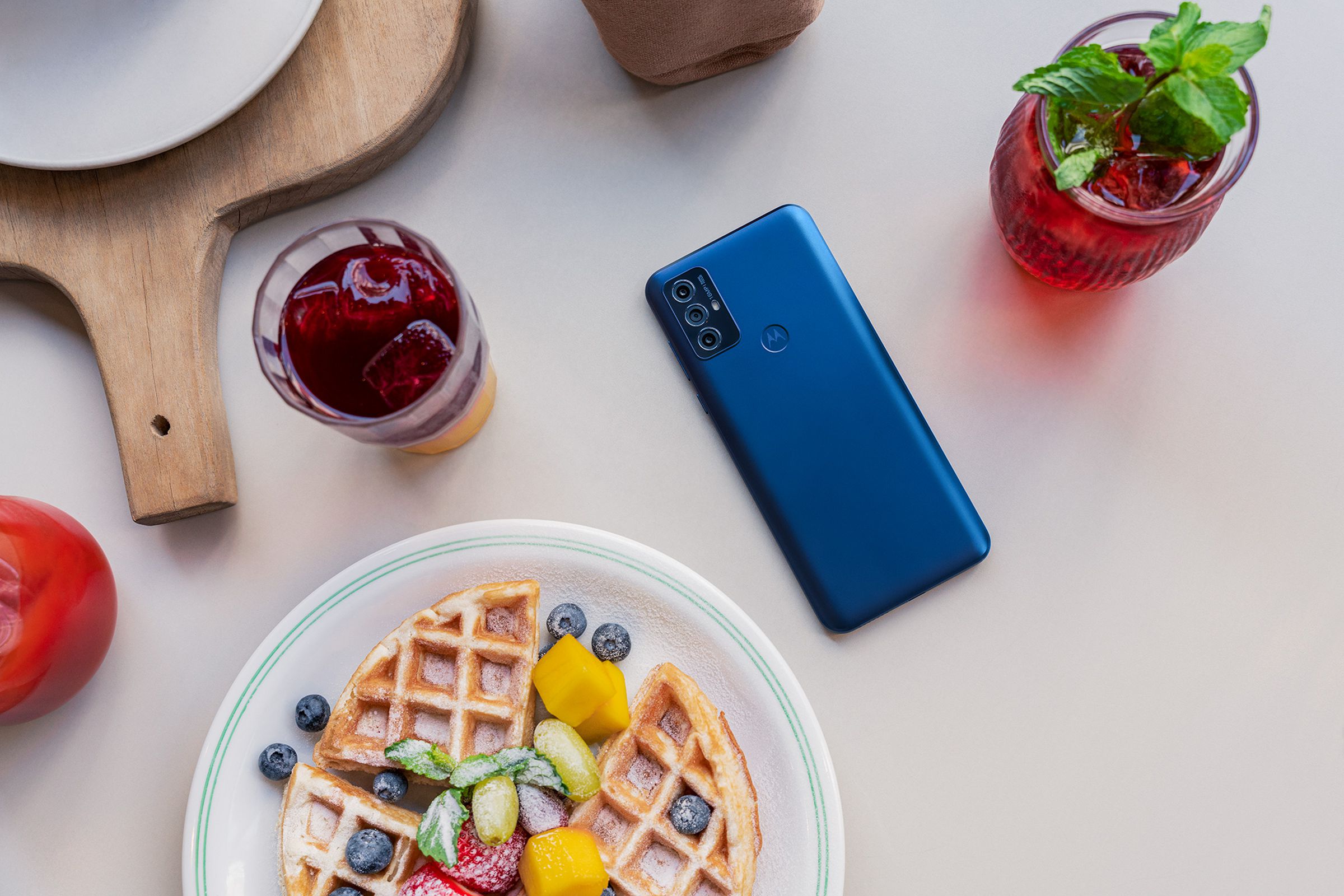 Motorola G Play, in blue, flat on a table with the rear facing up surrounded by breakfast plates and items.