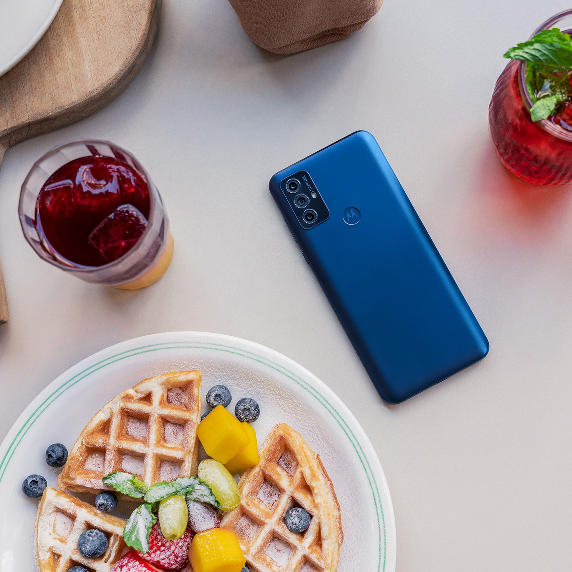 Motorola G Play, in blue, flat on a table with the rear facing up surrounded by breakfast plates and items.