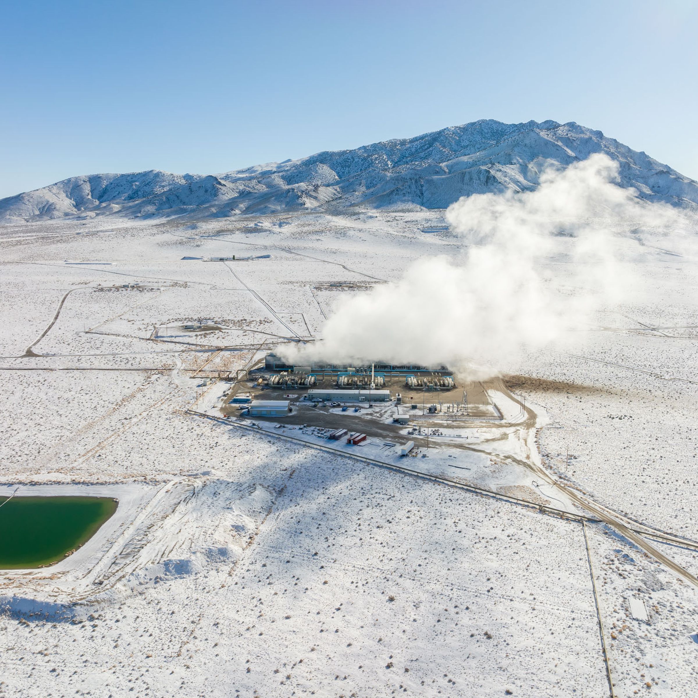 Steam rises from a geothermal power plant in the middle of a snow-covered desert.