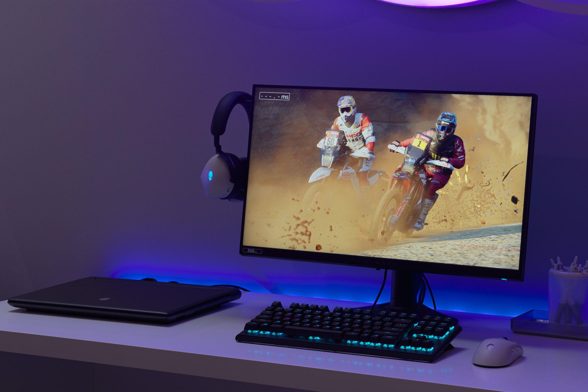 A desk with an Alienware AW2524H gaming monitor displaying two track motorbikes.