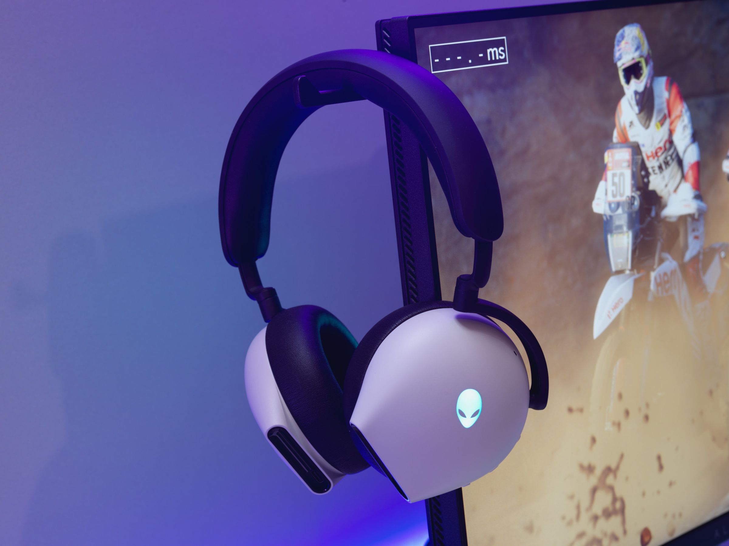 An Alienware gaming headset resting on the headset stand of an Alienware AW2524H gaming monitor.