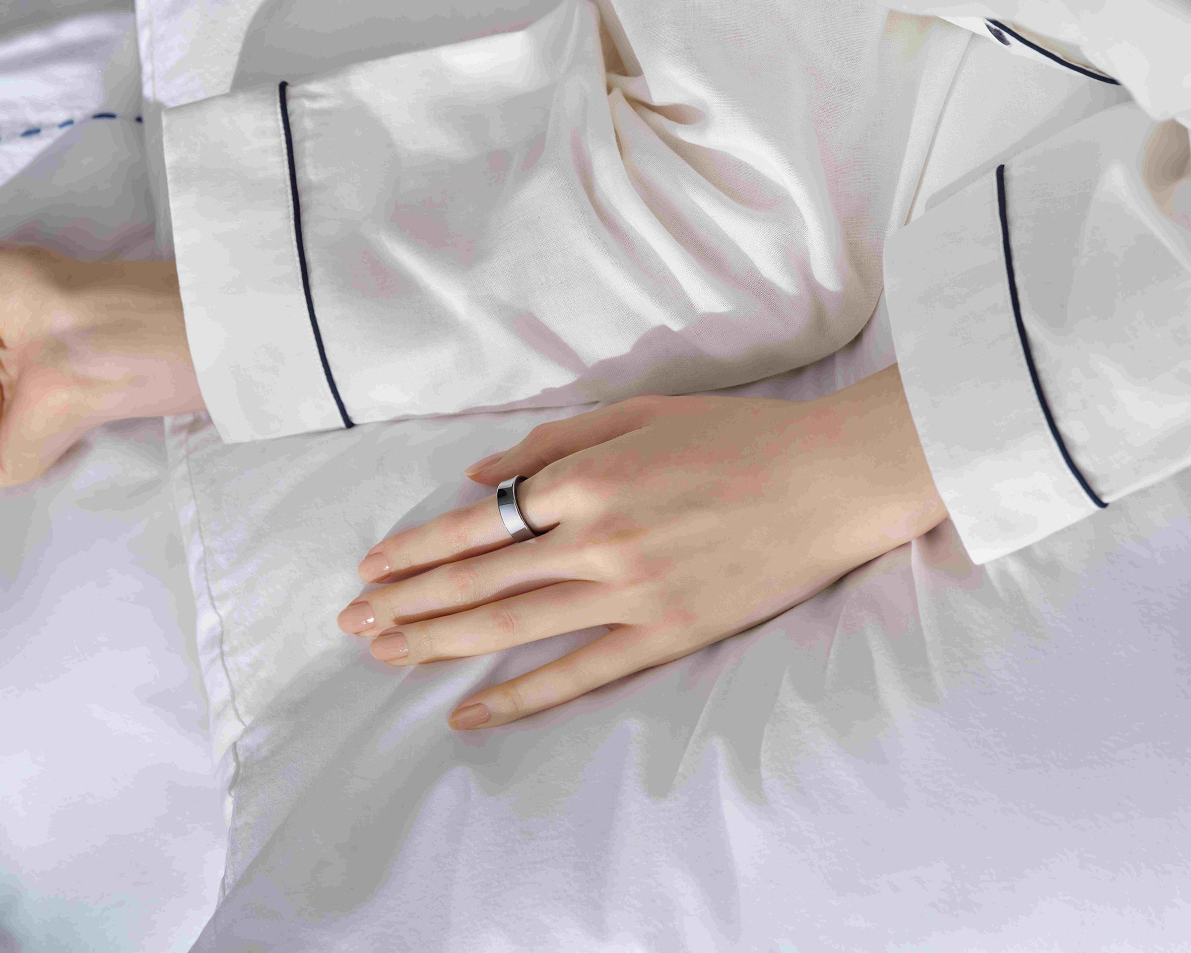 تصویر دست زن با حلقه گلکسی در حالی که فرد در رختخواب دراز کشیده است.