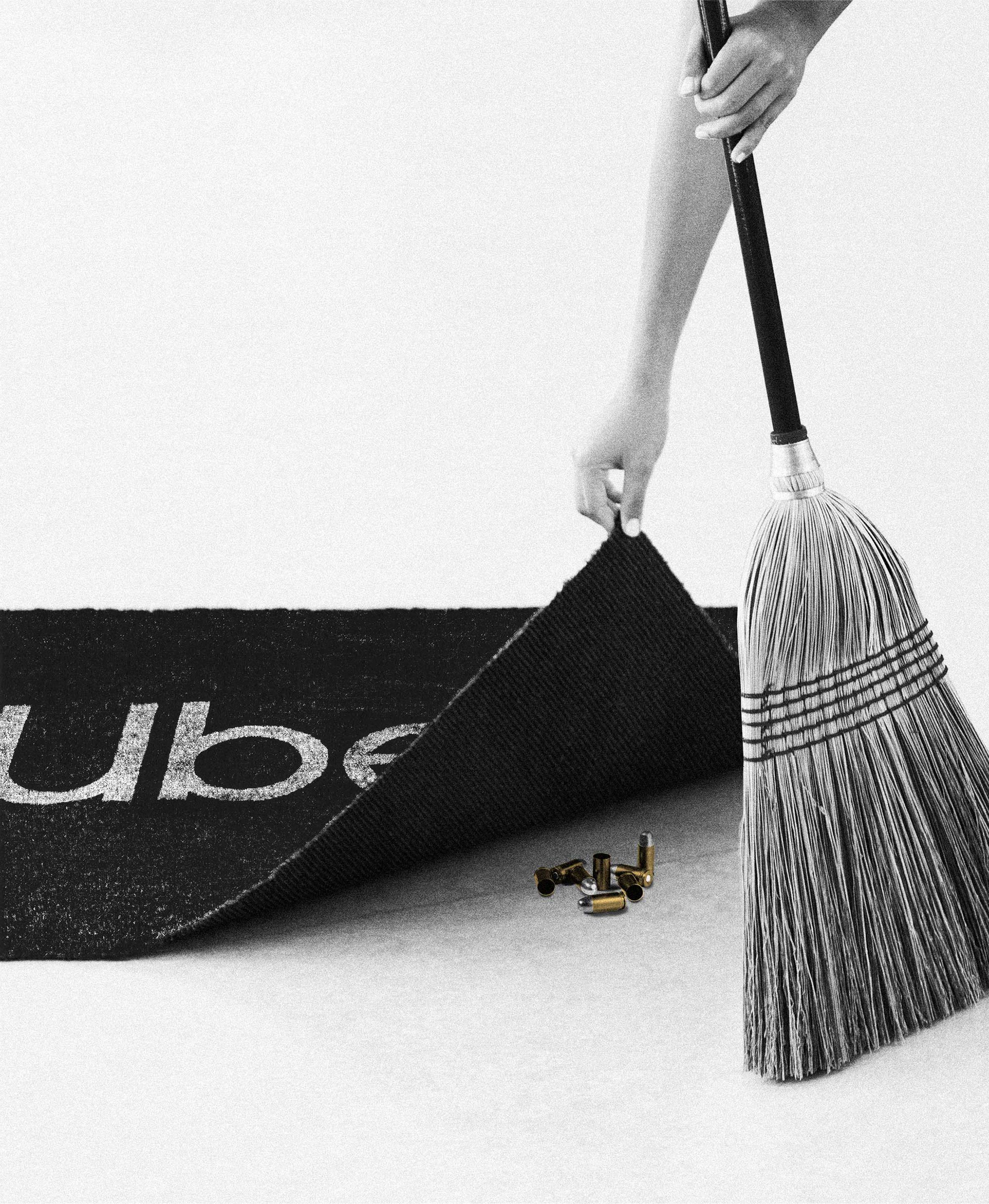 A broom sweeps bullets under a rug that says “Uber”