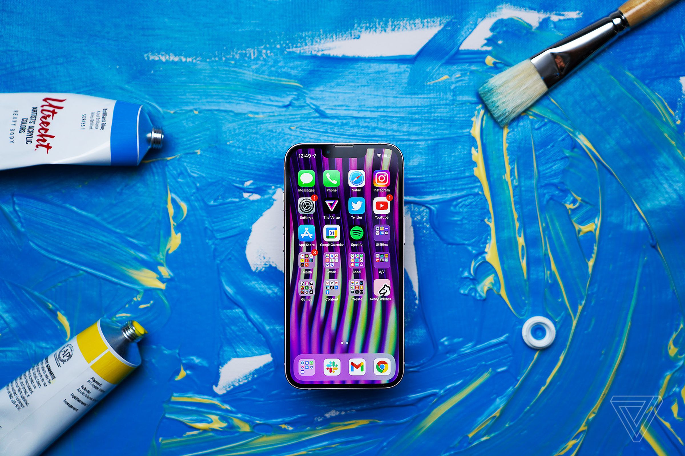 iPhone 13 on a background with blue paint splatter facing screen-side-up showing homescreen.
