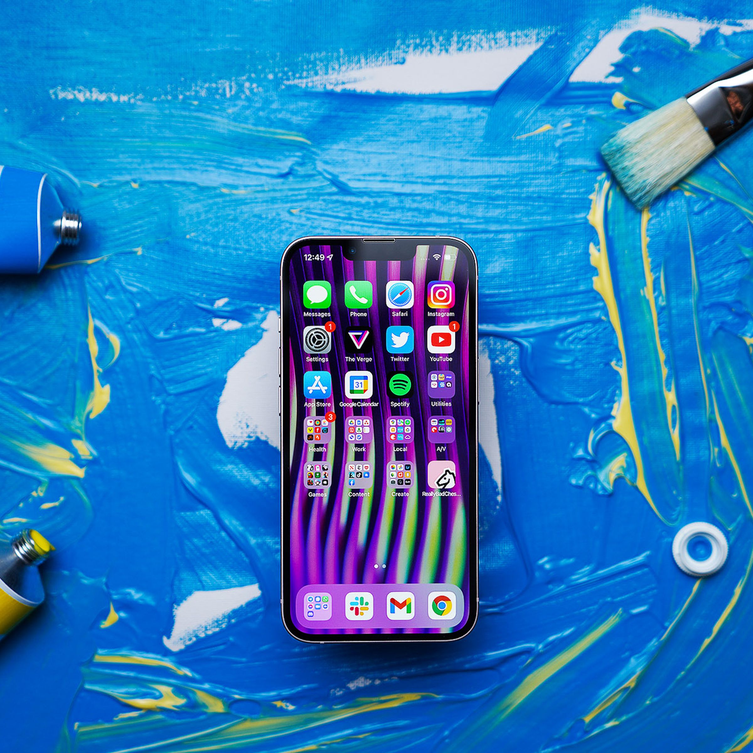 iPhone 13 on a background with blue paint splatter facing screen-side-up showing homescreen.