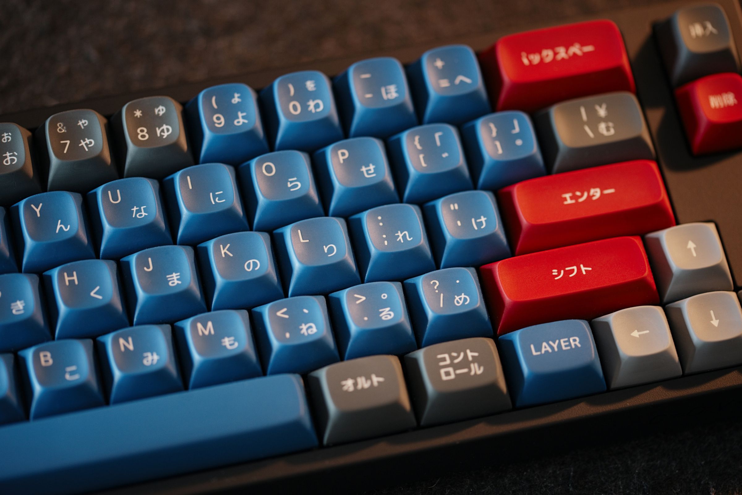 A close-up shot of a keyboard with blue alpha keys, a mixture of red and grey modifiers, and lighter grey arrow keys. The legends are a mix of Latin and Japanese characters.