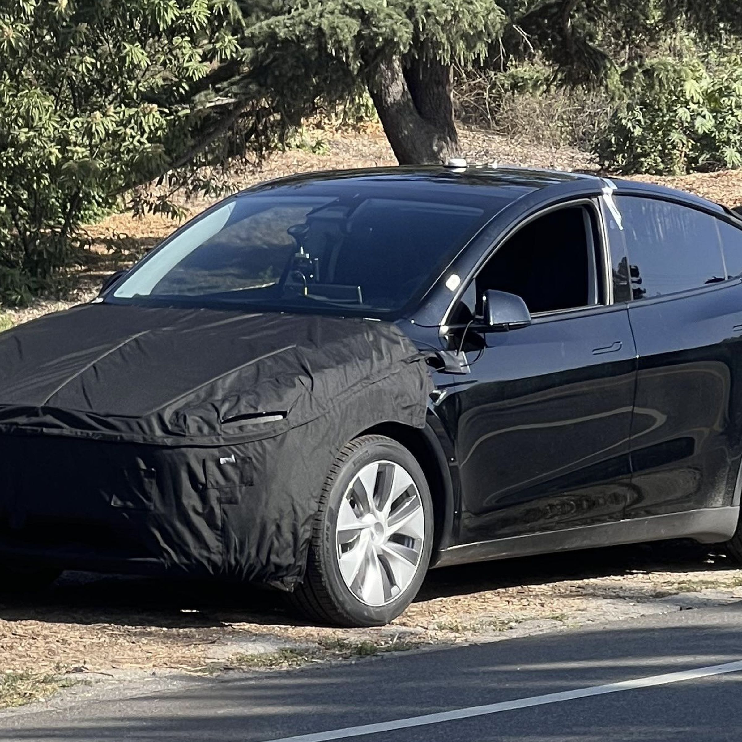 black model y SUV on the side of the Road with tarp on the front and back bumpers