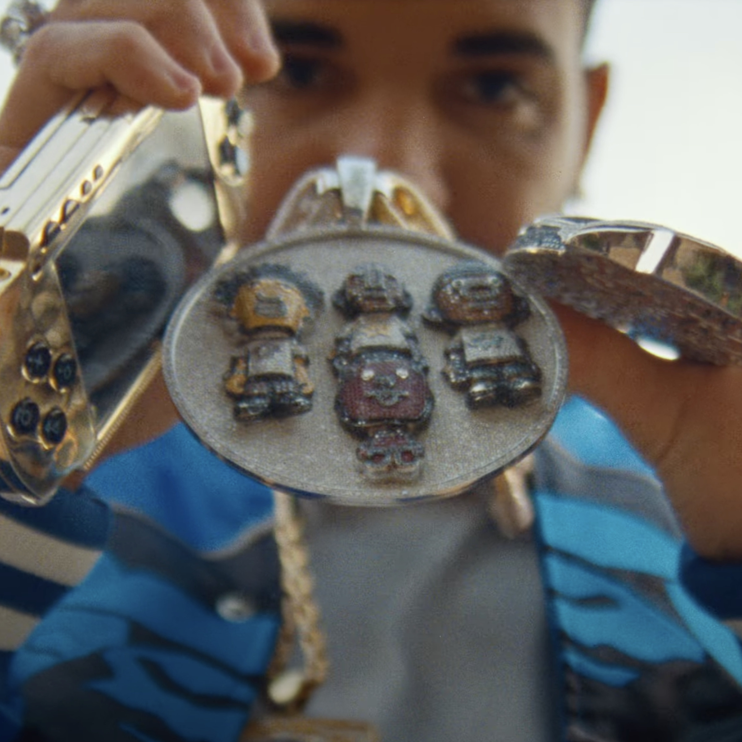 A close-up of a gold PSP and Pharrell Williams’ chains / medallions in the hands of Drake, who is holding it all right in front of his face.
