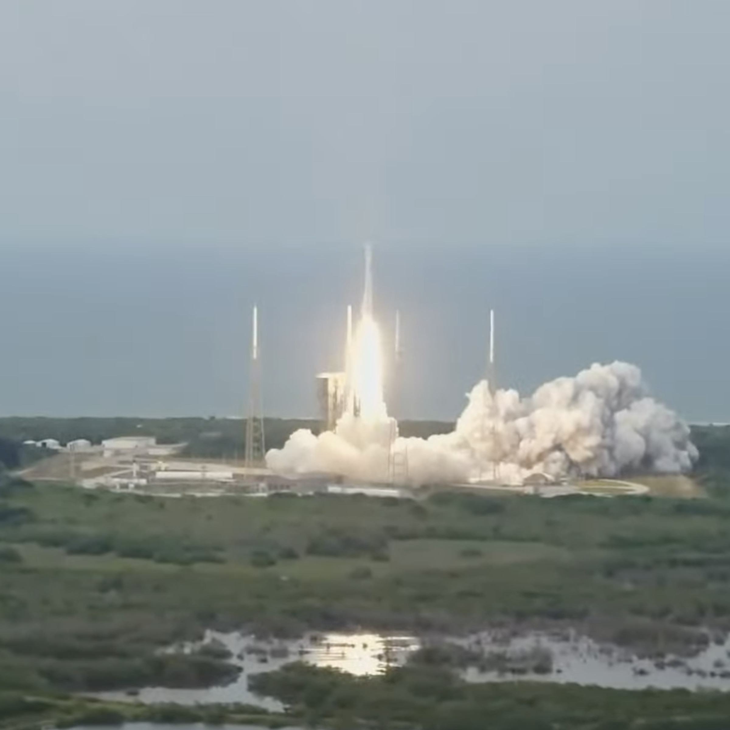 A rocket taking off on a cloudy day with a swamp in the foreground