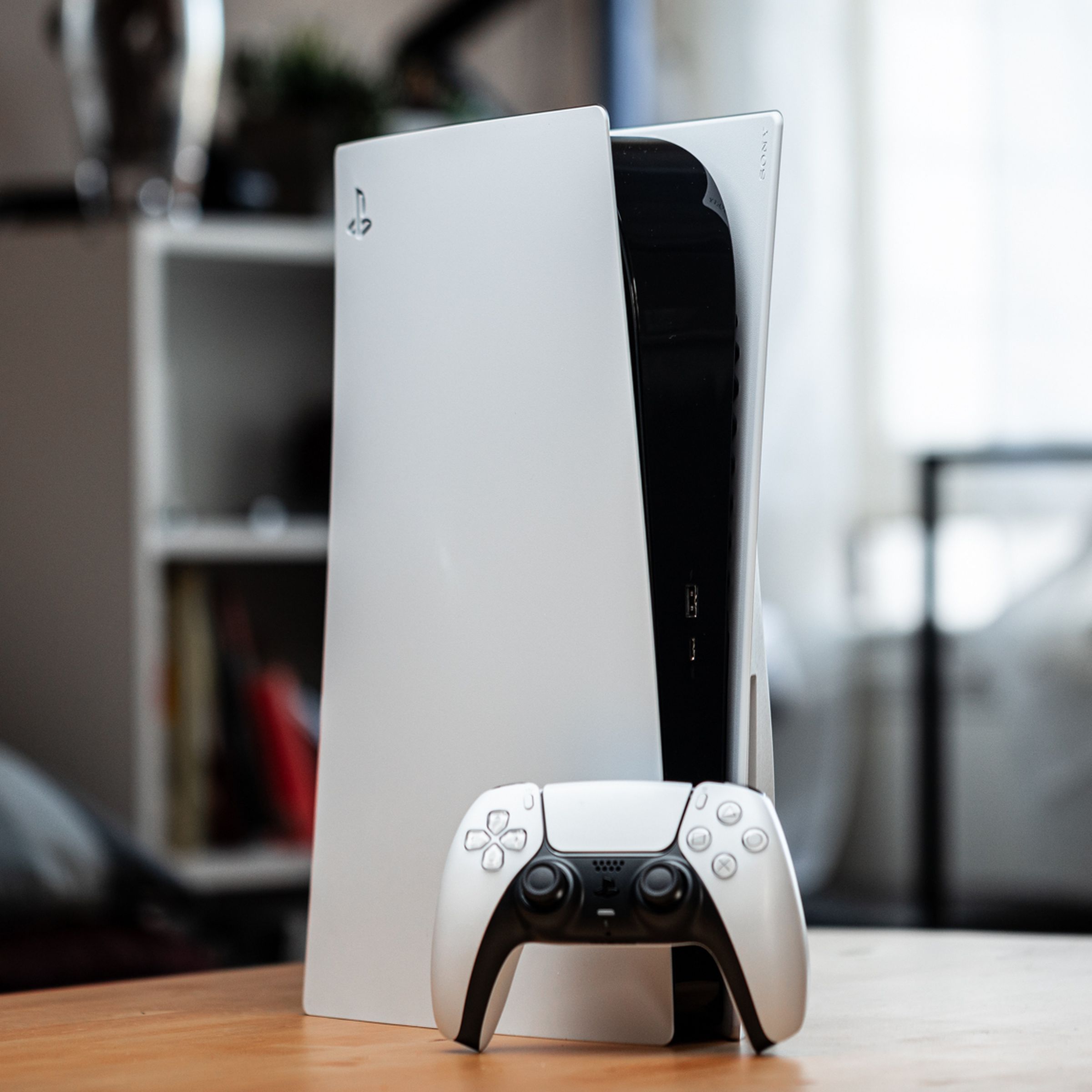 A picture of the PlayStation 5 on a table, with a DualSense controller leaning against it.