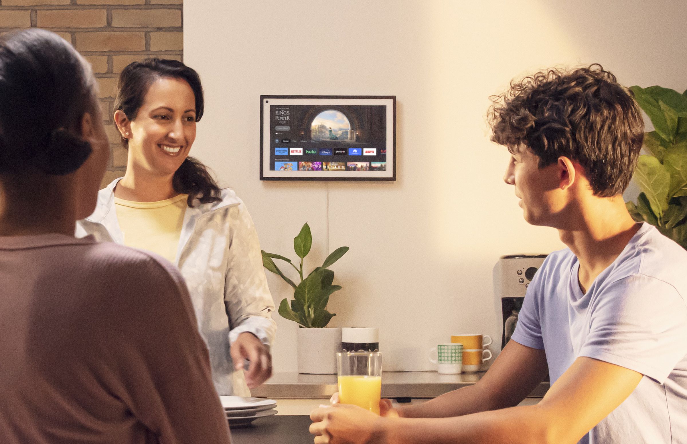 An image of an Echo Show 15 mounted to a wall running Amazon’s Fire TV OS. People are in the foreground having a conversation.