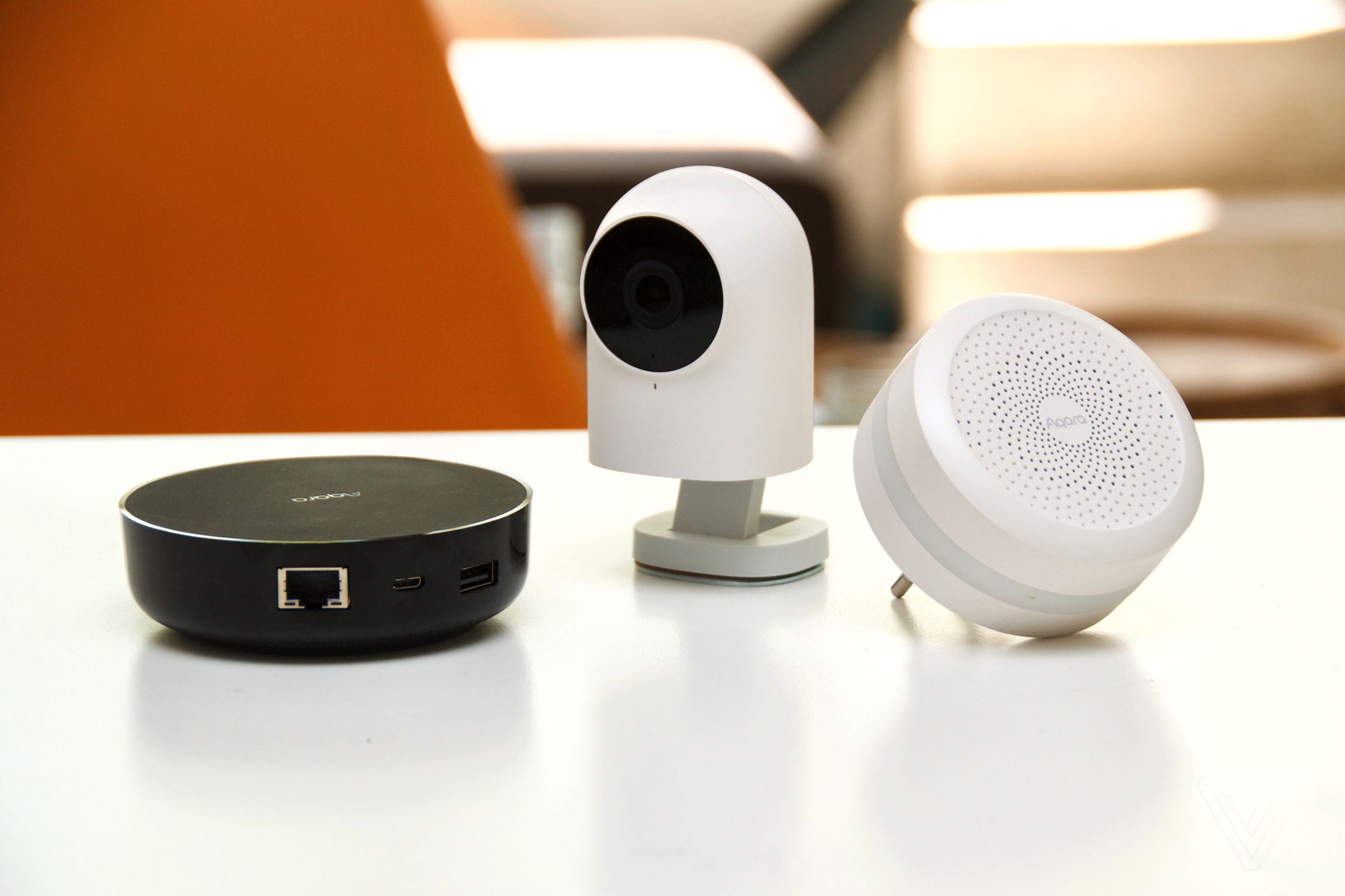 Three Aqara smart home devices on a white table. An orange chair is in the backdrop.