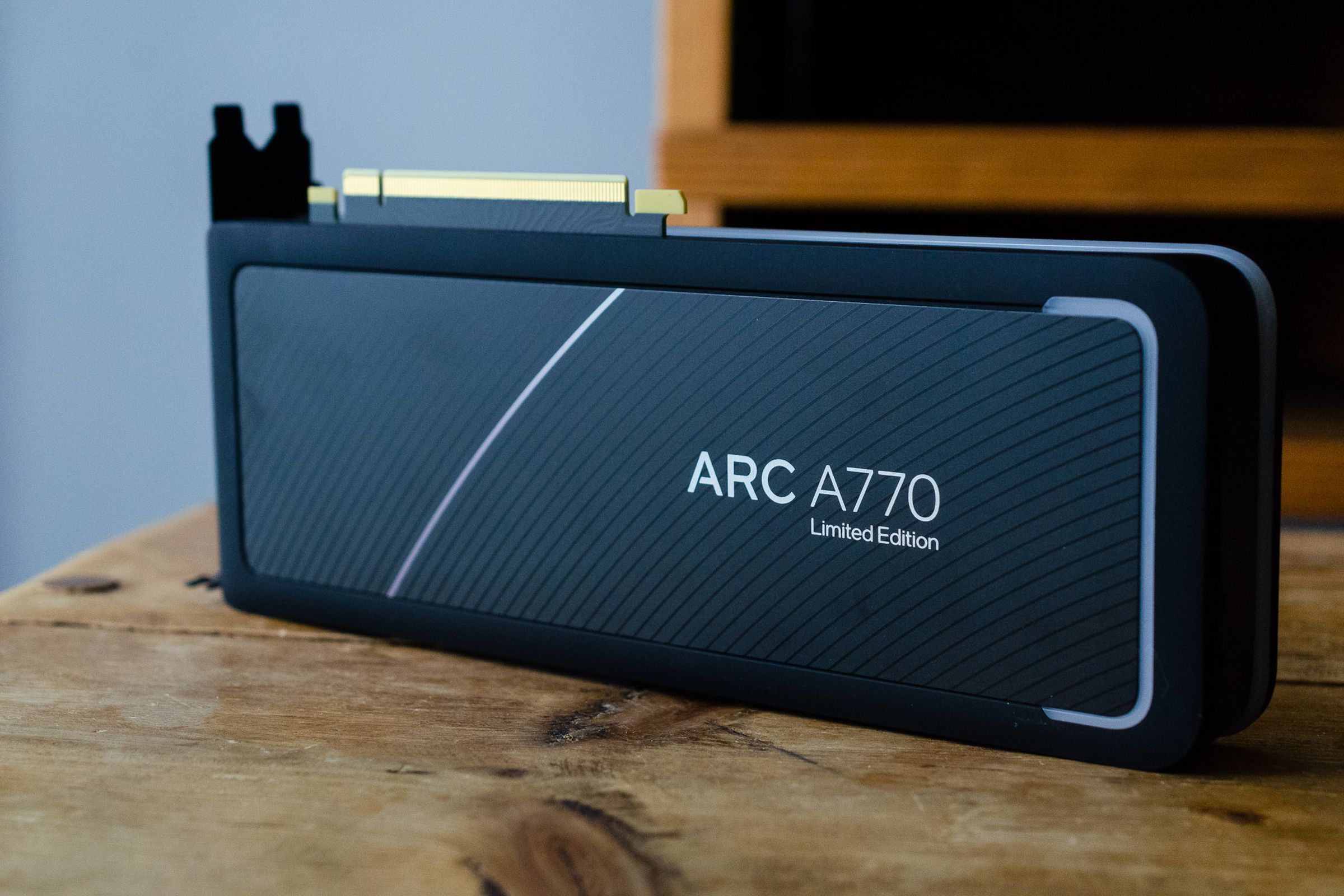 Intel’s new Arc A770 GPU sitting on a wooden table, with its matte black finish and rounded edges