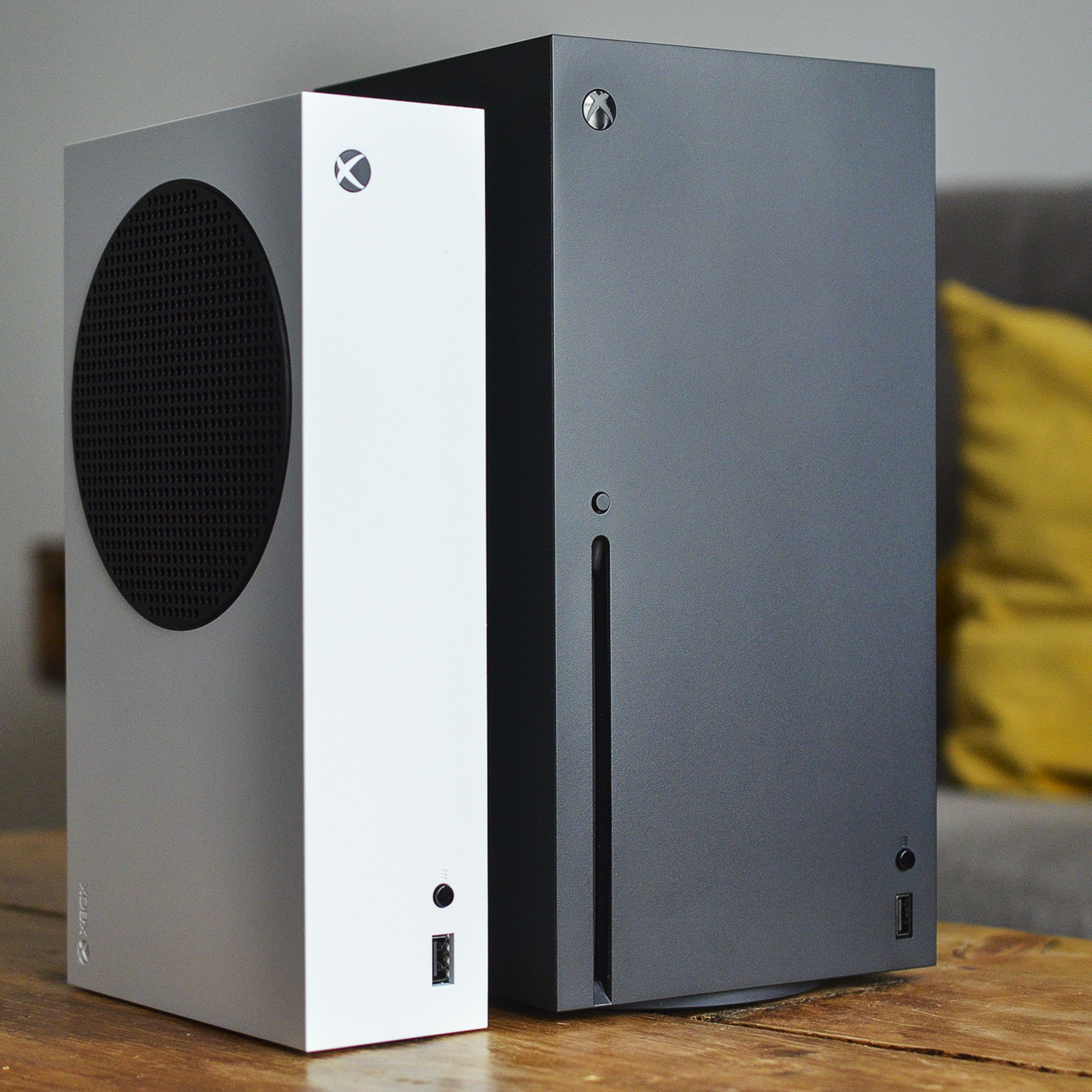 Microsoft’s white Xbox Series S sits alongside a bigger black Xbox Series X on a wooden coffee table in a living room