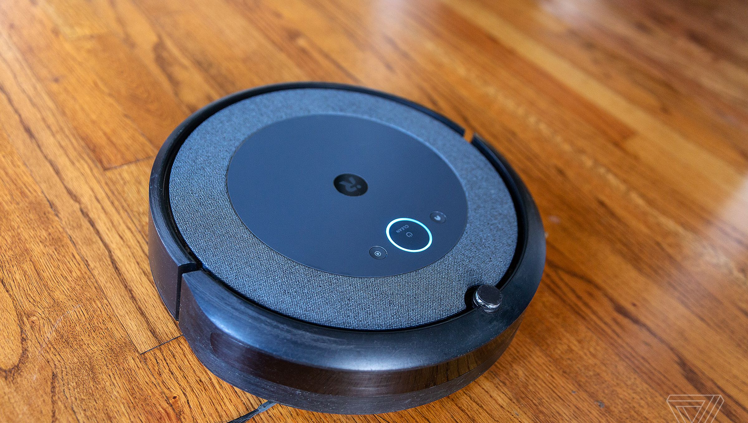 The iRobot Roomba i3 Plus EVO robotic vacuum cleaner lies on a wooden floor.