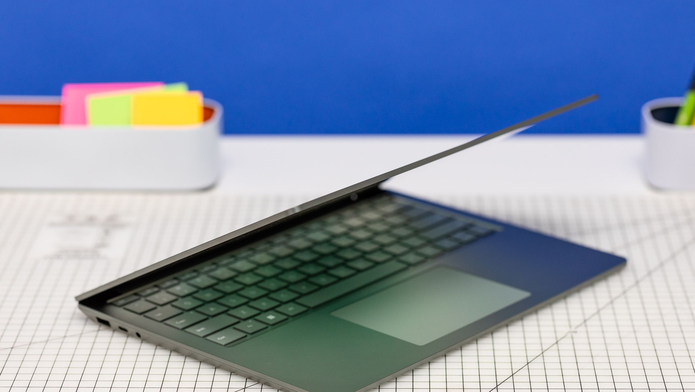 The Surface Laptop 5 half open on a gridded table with post-it notes in the background.