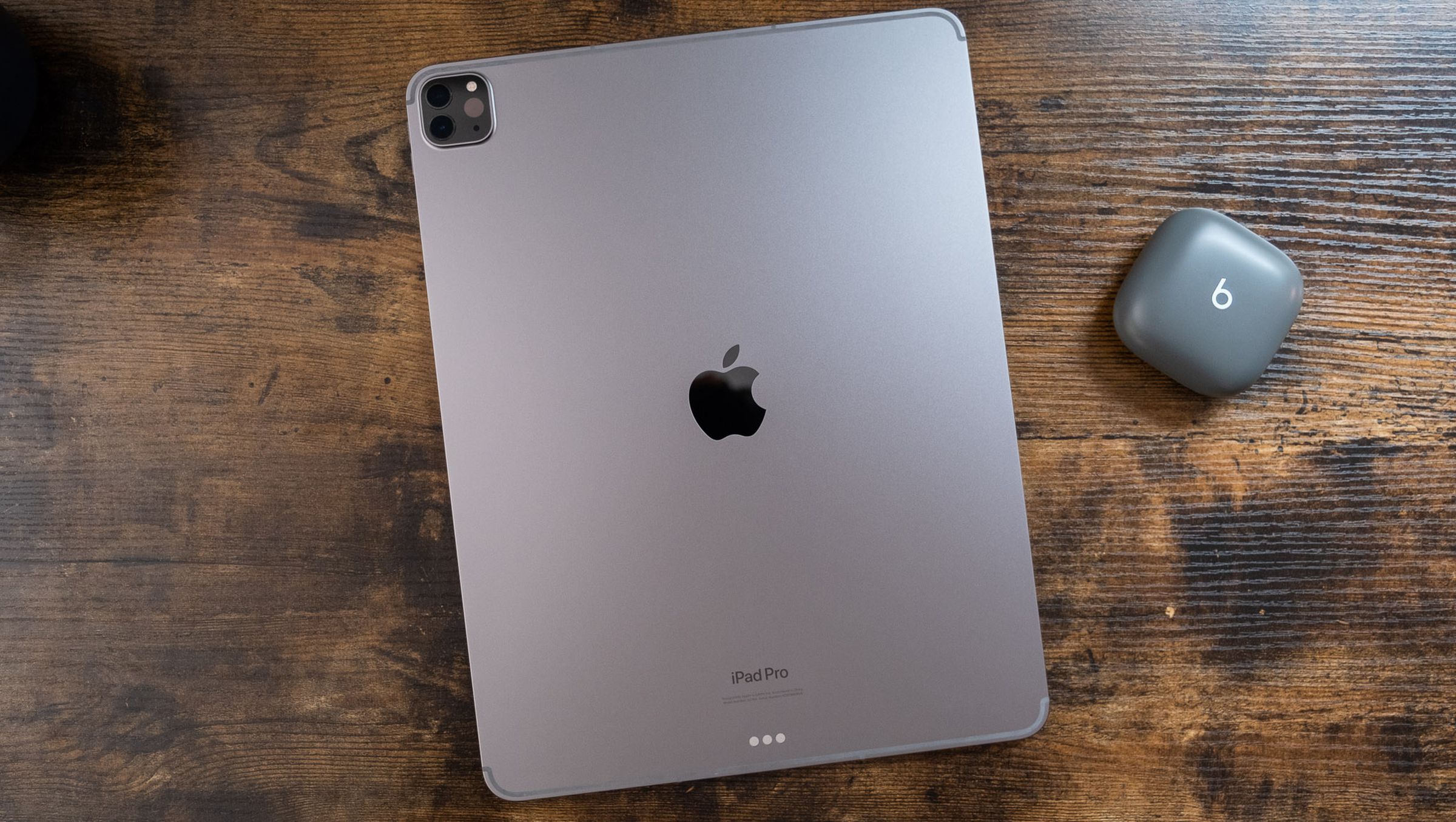 A 12.9-inch space gray iPad Pro face down on a wooden table, viewed from the top down.