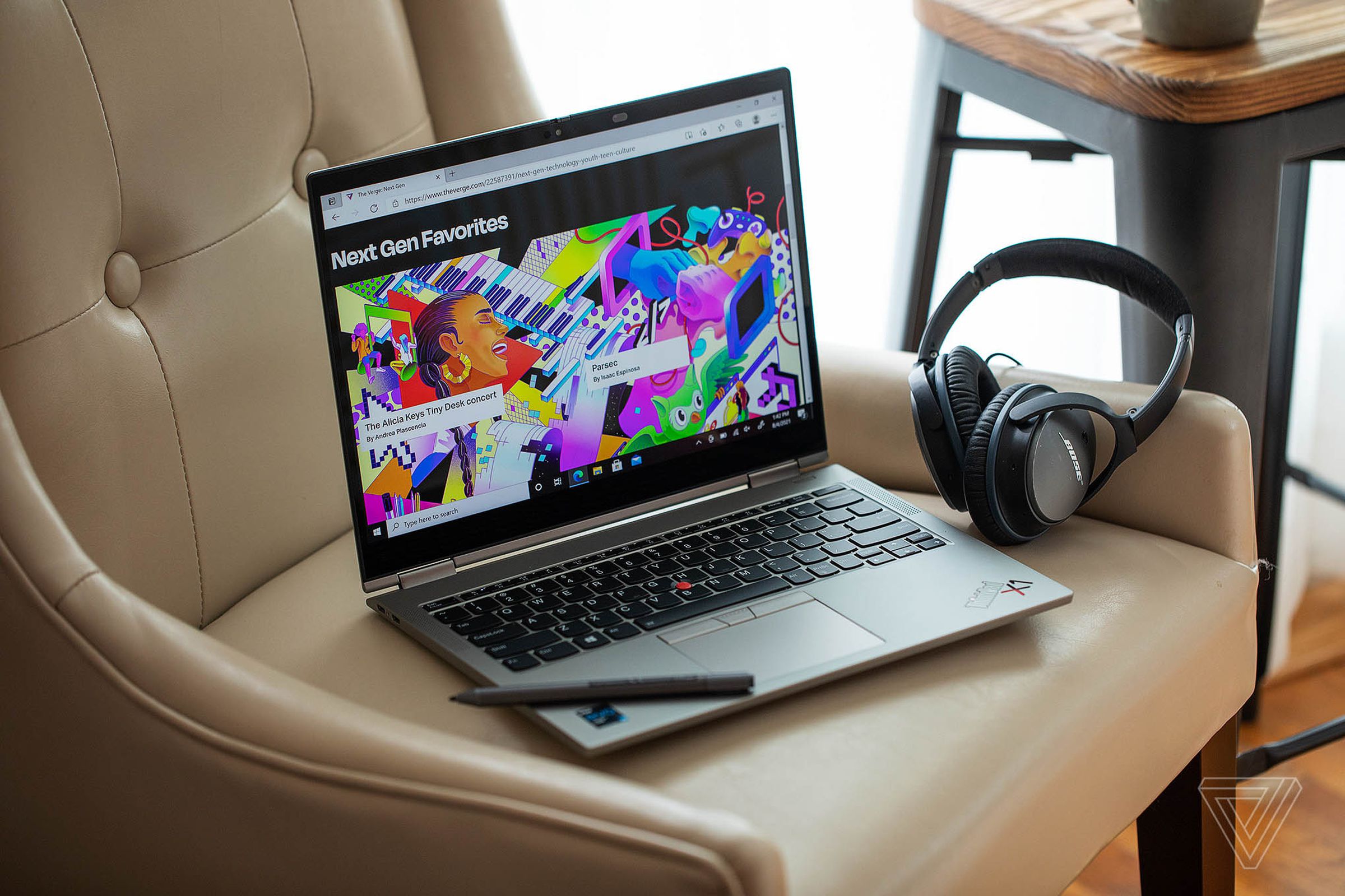 The Lenovo ThinkPad X1 Titanium Yoga on an armchair, open, angled to the right, seen from above with the stylus diagonally acorss its left palm rest and a pair of black headphones to its right side.