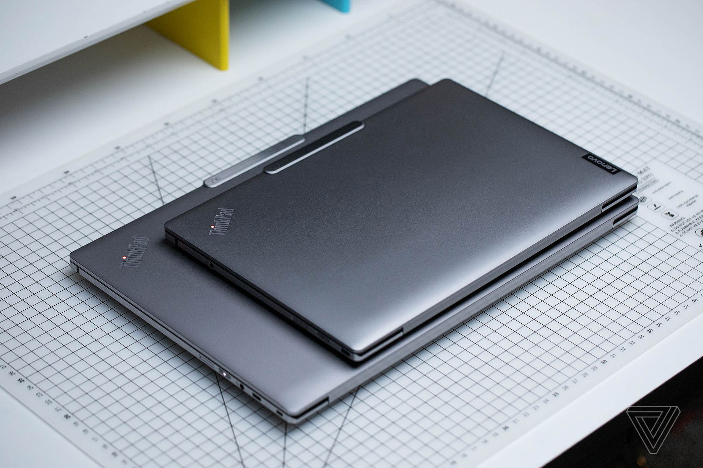 The Lenovo ThinkPad Z13 on top of the Lenovo ThinkPad Z16, both closed atop a gridded table.