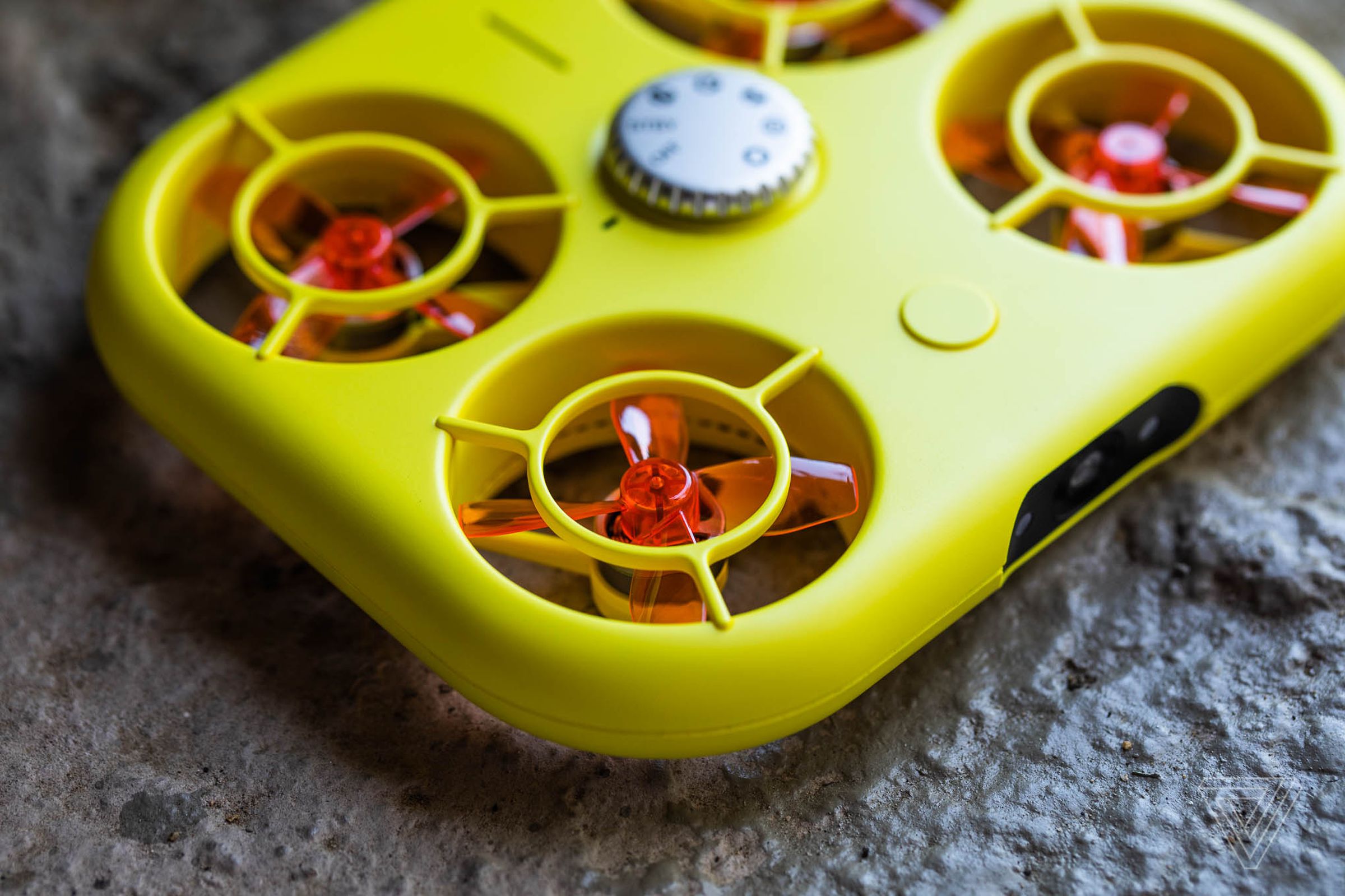 A yellow drone shaped like a rounded rectangle instead of exposed blades — it has translucent orange propellers within its boxy but thin frame.