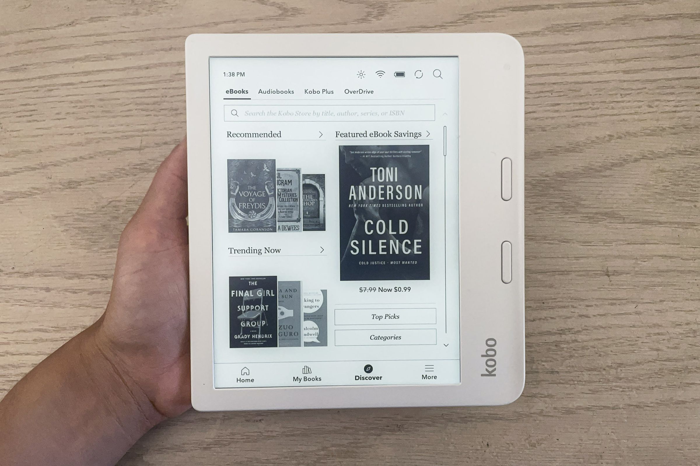 A hand holding up the Kobo Libra 2 turned on with its home screen on display.